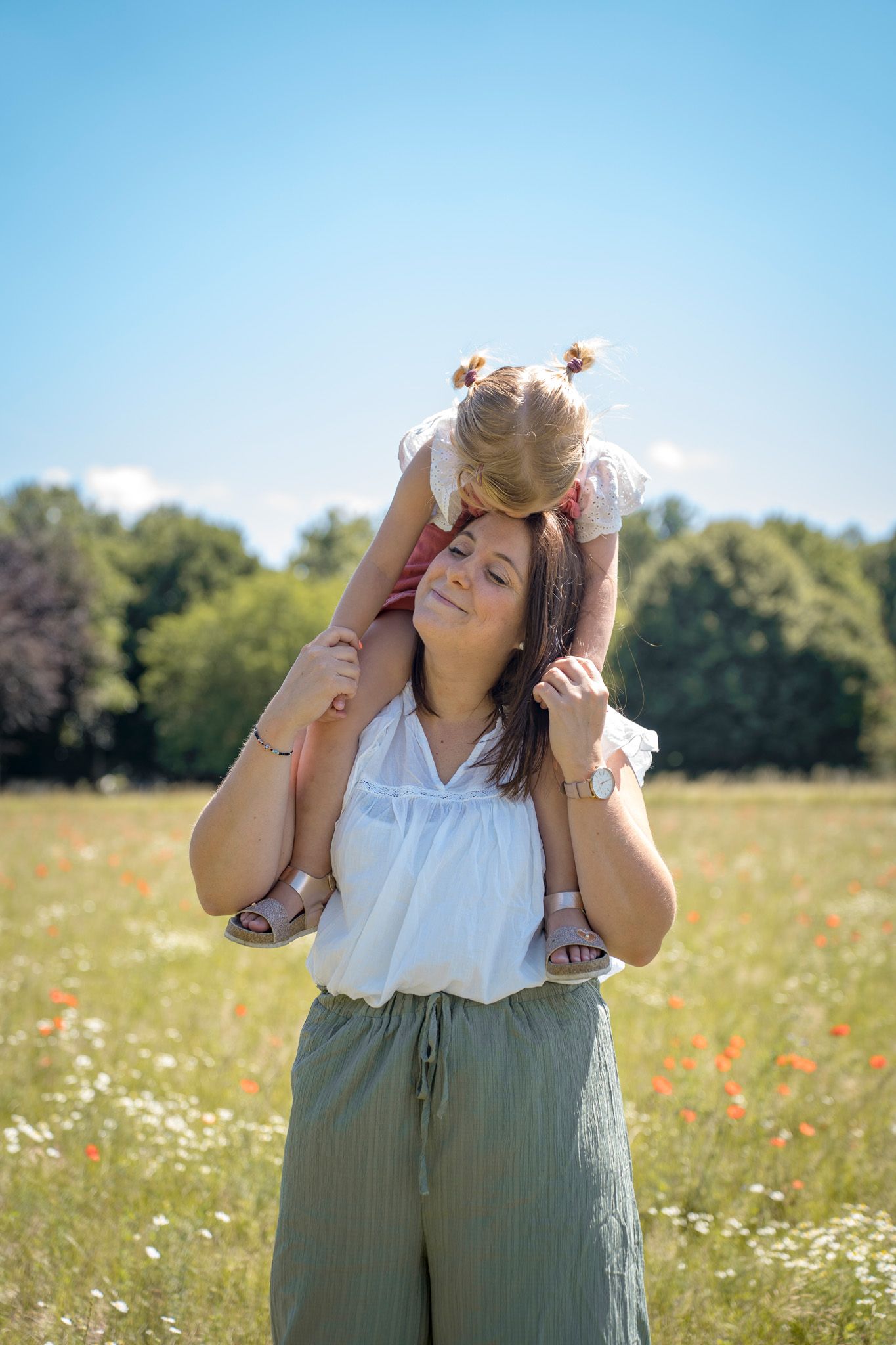 A person in a white top and olive pants stands in a sunny wildflower meadow on a bright summer day.