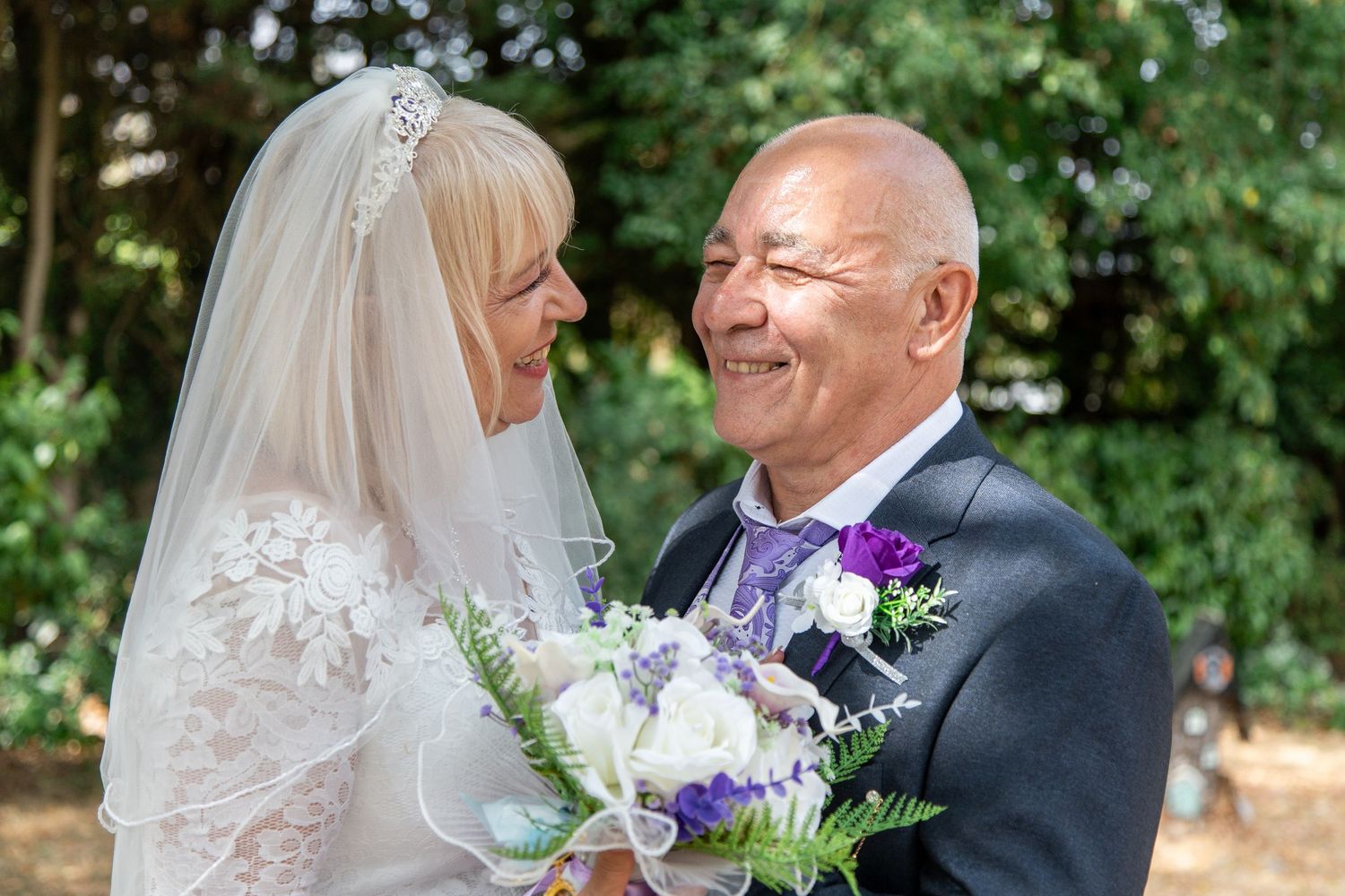 Joyful older bride and groom sharing a romantic moment outdoors, bride holding purple and white bouquet.