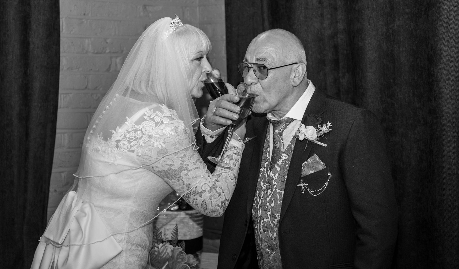 Black and white photo of a bride and groom sharing a champagne toast at their wedding reception.