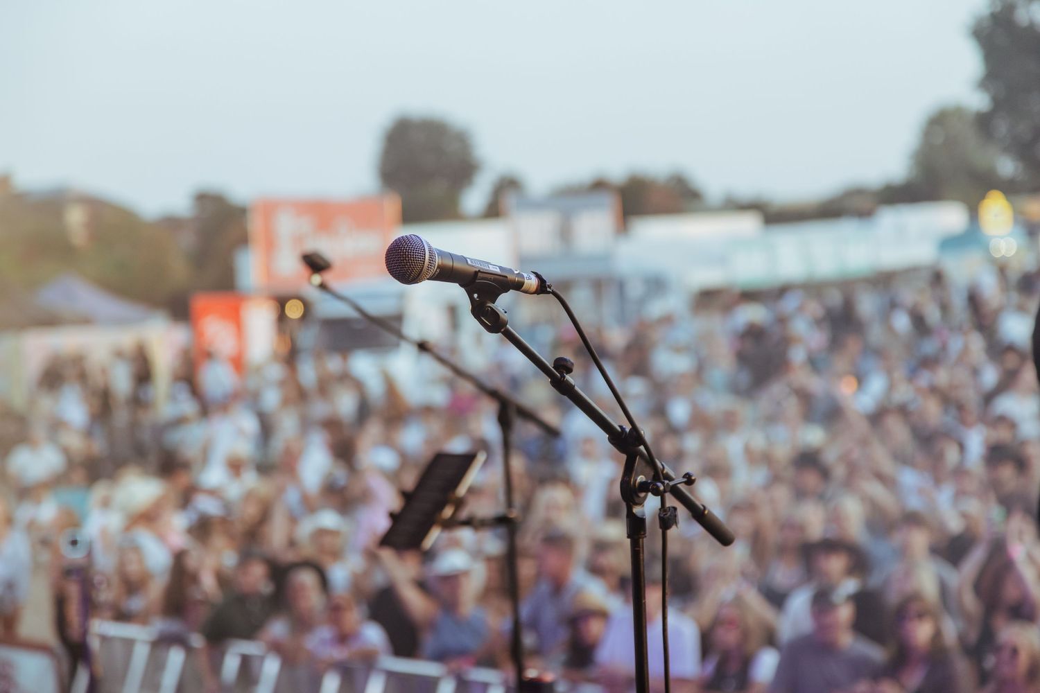A microphone on a stand in focus at an outdoor concert with a large blurred crowd in the background.