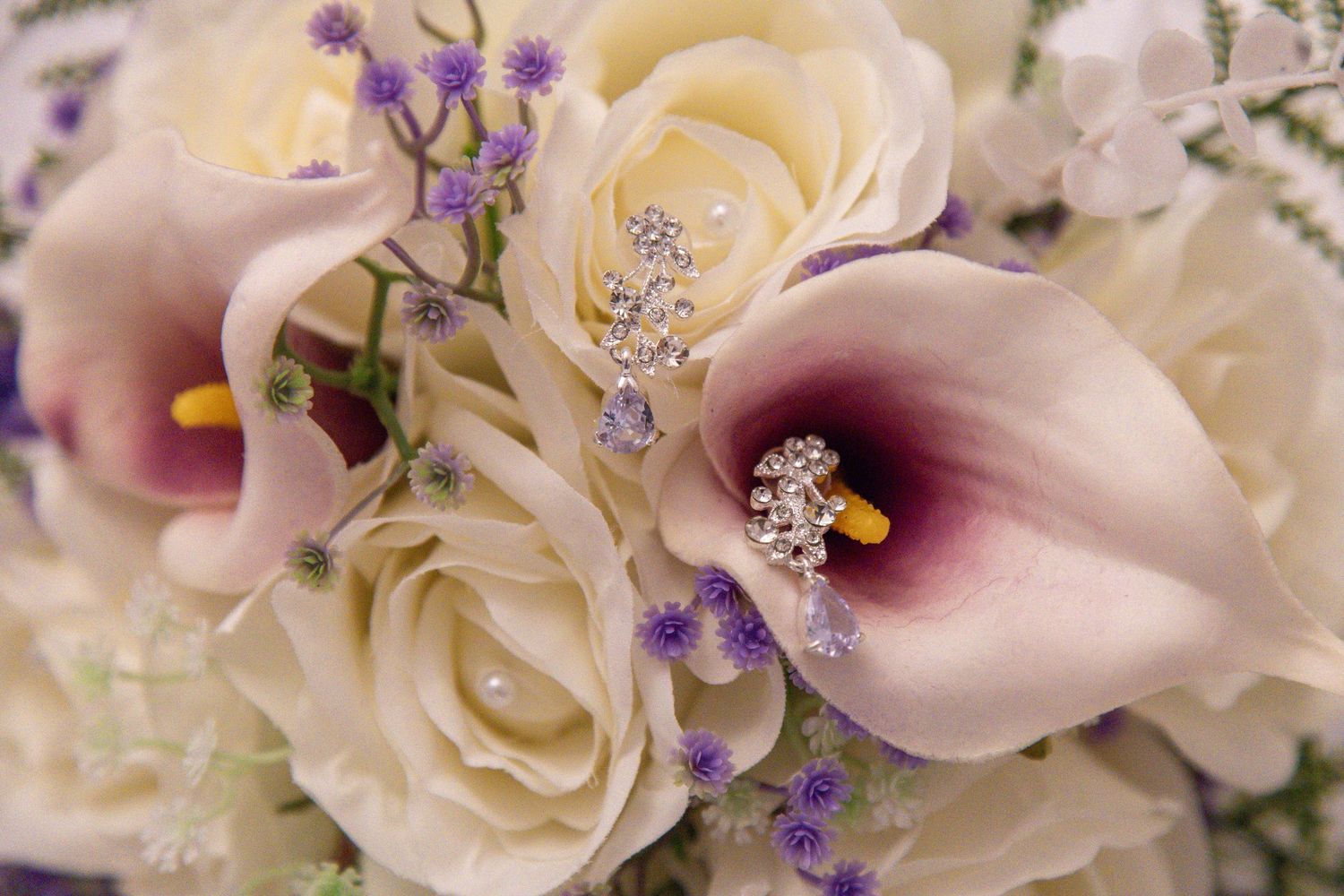 Close-up of a bridal bouquet featuring purple calla lilies, cream roses, and delicate lavender wildflowers with pearl accents.