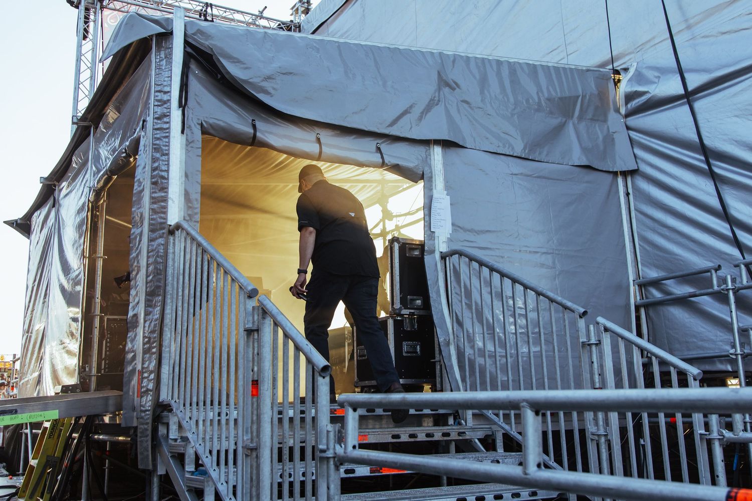 Worker setting up backstage area with metal railings and gray tarpaulin at an outdoor event venue.