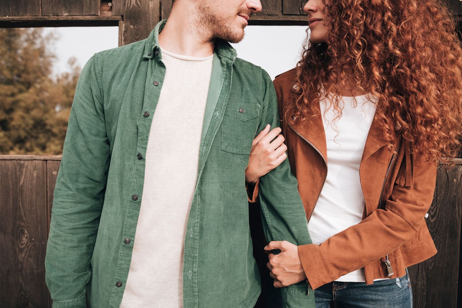 A couple in autumn clothing shares a romantic moment outdoors with green and brown tones in their outfits.