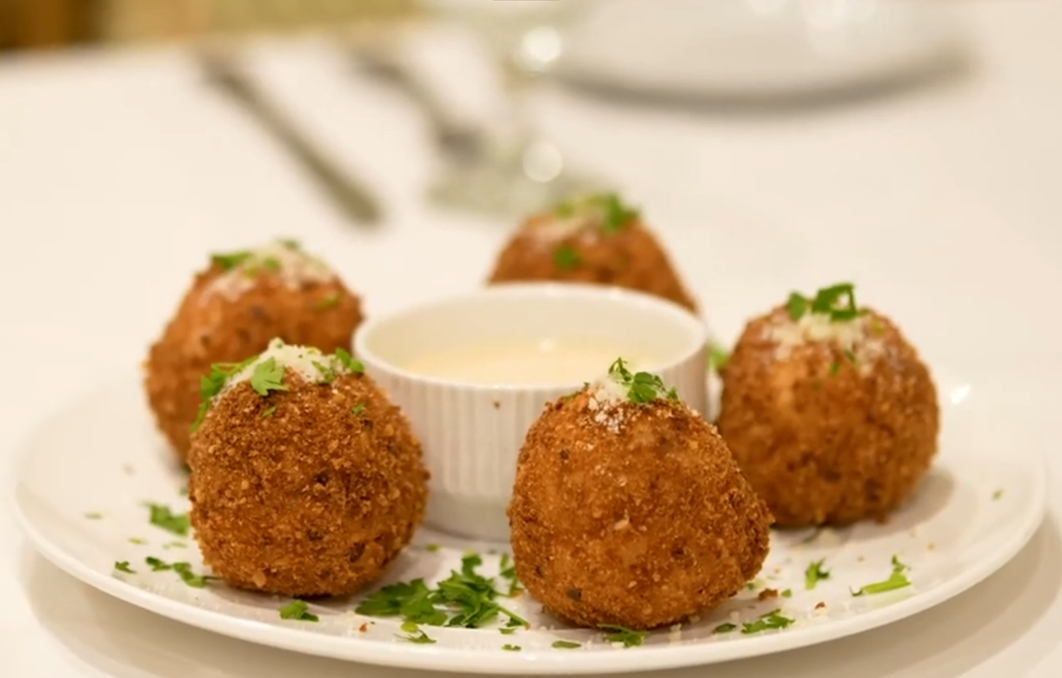 Golden fried arancini balls served with creamy dipping sauce, garnished with fresh herbs on a white plate.