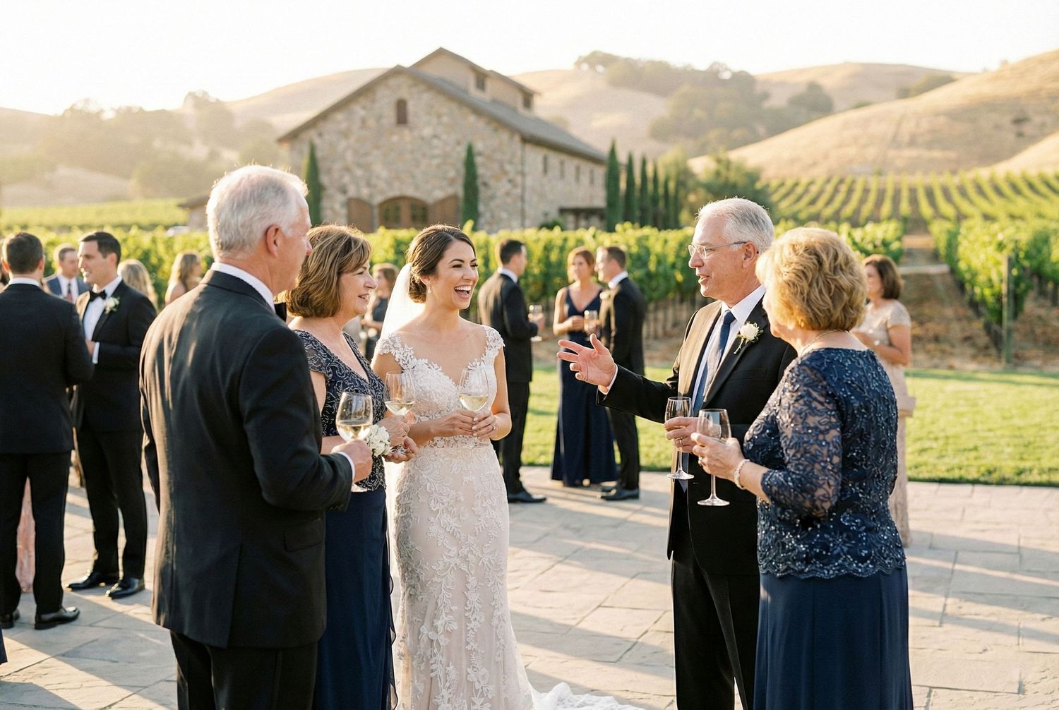 Bride in lace gown mingles with guests holding champagne at a sunny vineyard wedding reception in California.