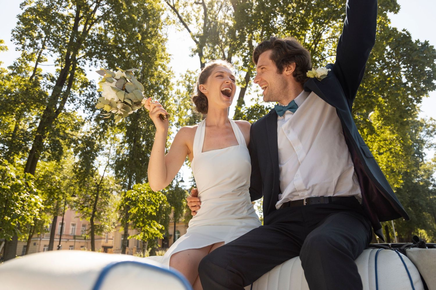 A couple in wedding attire dances together outdoors under sunlit trees during their special celebration.