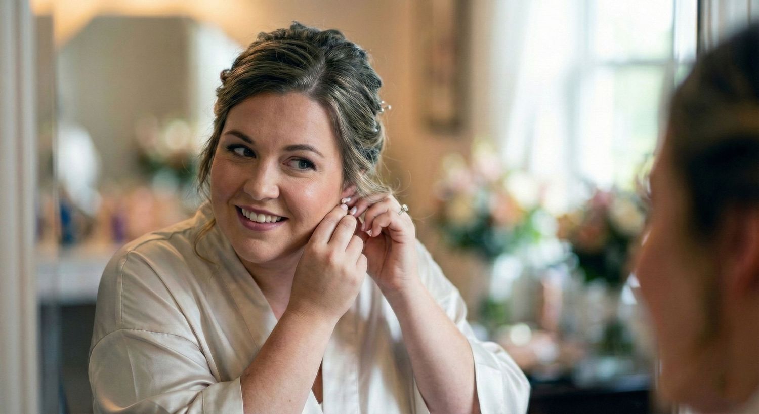 Bride smiling while putting on earrings during wedding preparations in elegant bridal suite.