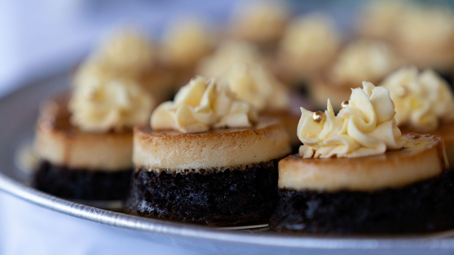 Elegant mini cheesecakes topped with swirled buttercream frosting on chocolate bases, served on a silver platter.