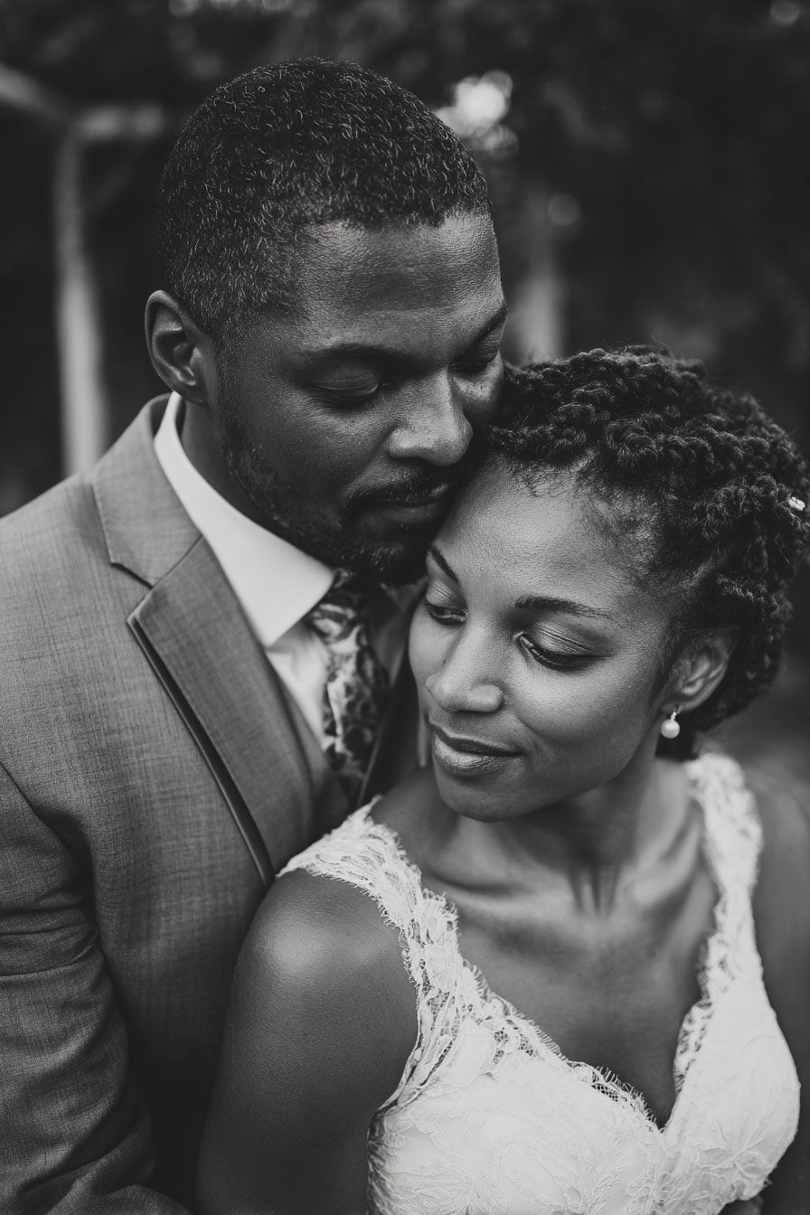 Black and white wedding portrait of a couple embracing tenderly, groom in gray suit, bride in lace dress.