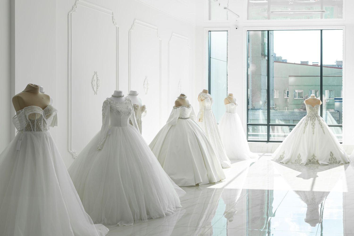 Elegant white wedding dresses displayed on mannequins in a bright, modern bridal boutique showroom.