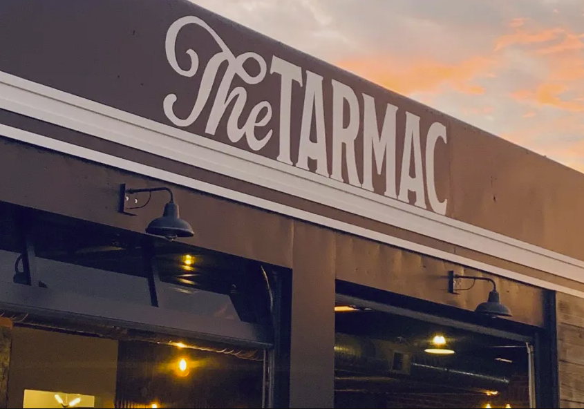 The Tarmac restaurant exterior sign illuminated at dusk with warm sunset sky in the background.
