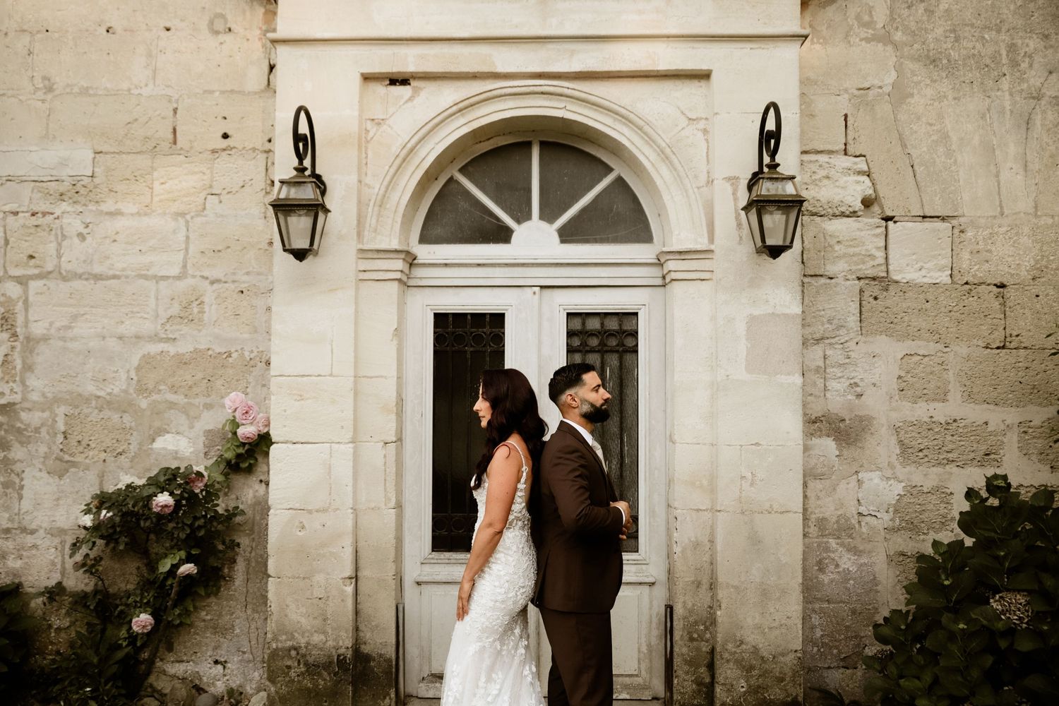 A couple shares a romantic moment outside a historic stone building with an arched doorway and lantern.