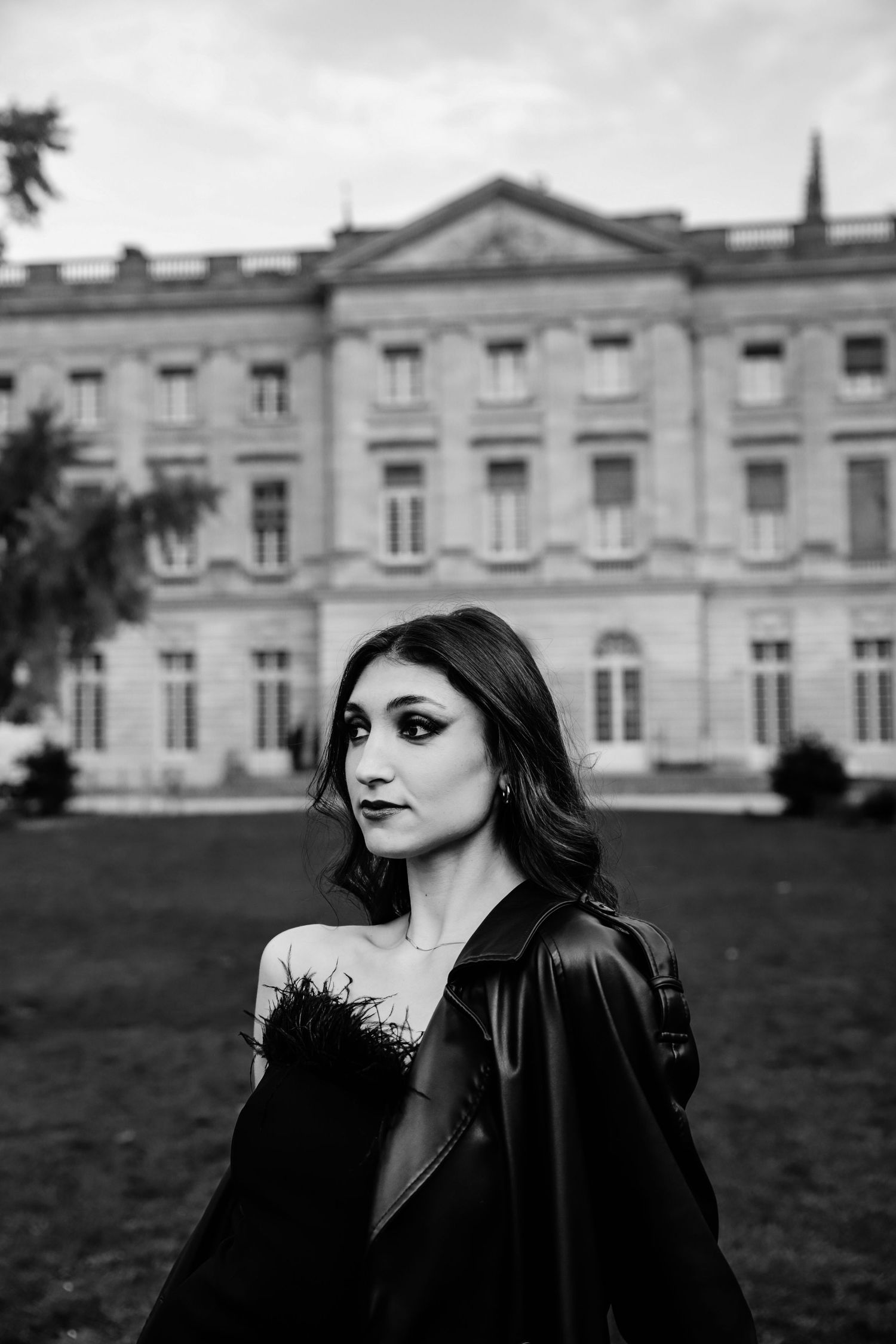 Black and white portrait of a young woman in leather jacket standing before a grand historic building.