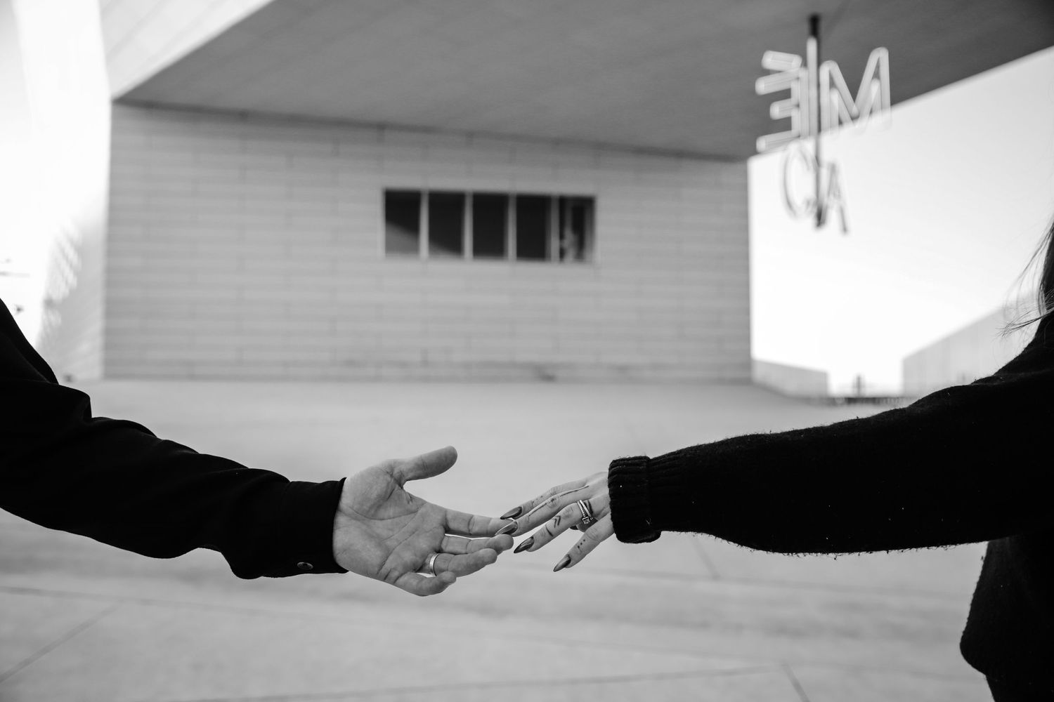 Black and white photo of two people reaching out to shake hands outdoors near a building.