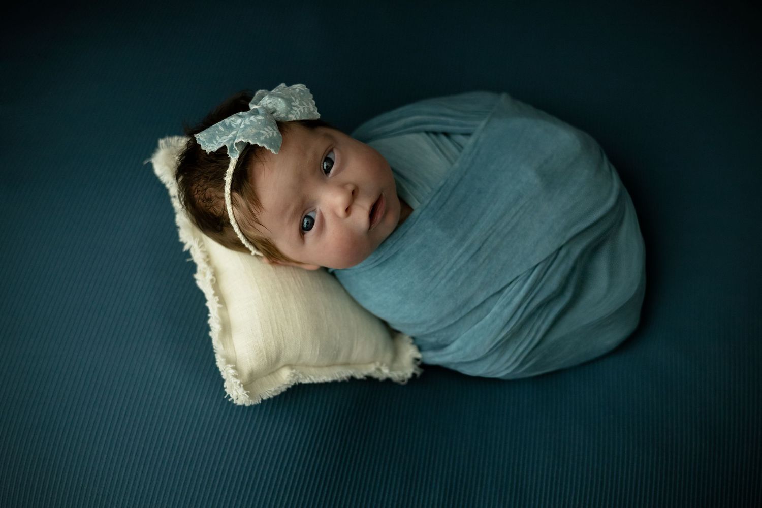 Baby girl swaddled in blue laying on a cream-colored pillow by Little Buckaroo Portrait Co., an East Texas Newborn Photographer