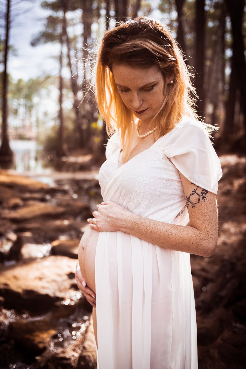Young pregnant woman in white dress standing by a creek in photo taken by Little Buckaroo Po