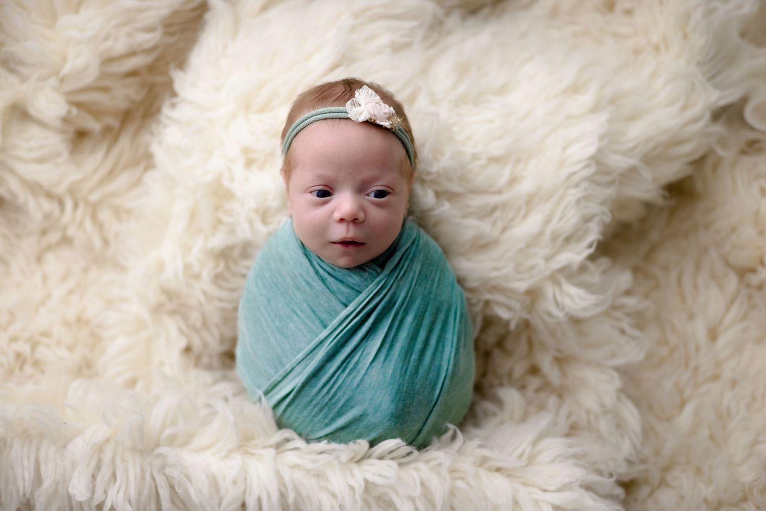 Swaddled newborn girl in white fur in photo taken by Little Buckaroo Portrait Co. in East Texas