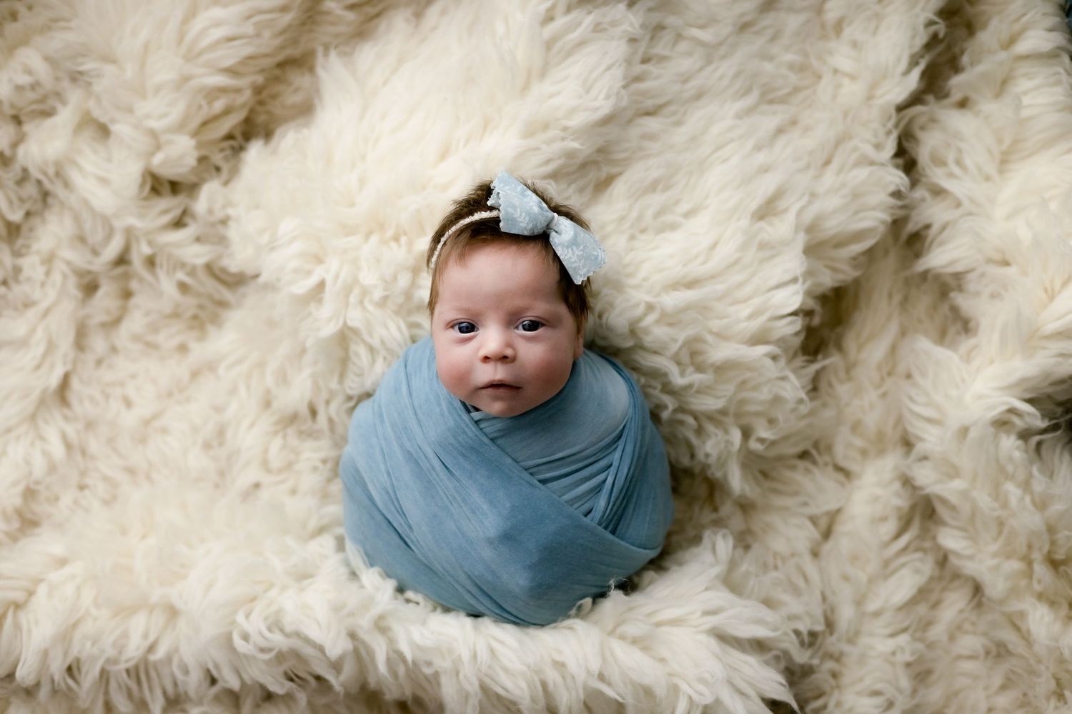 Swaddled newborn girl in white fur in photo taken by Little Buckaroo Portrait Co. in East Texas