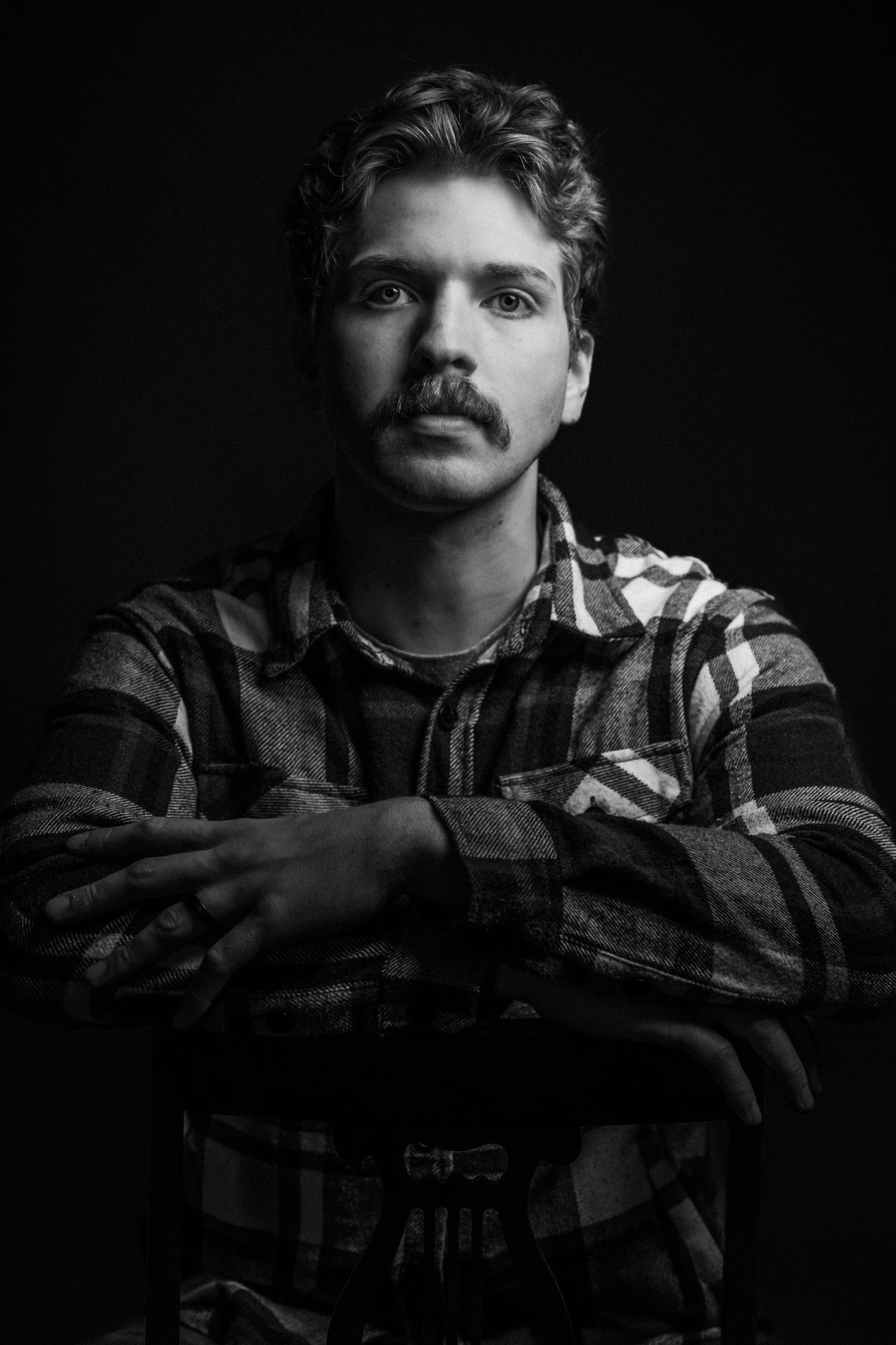 Black and white portrait photograph of a person wearing a plaid shirt with crossed arms in a dramatic lighting setup.