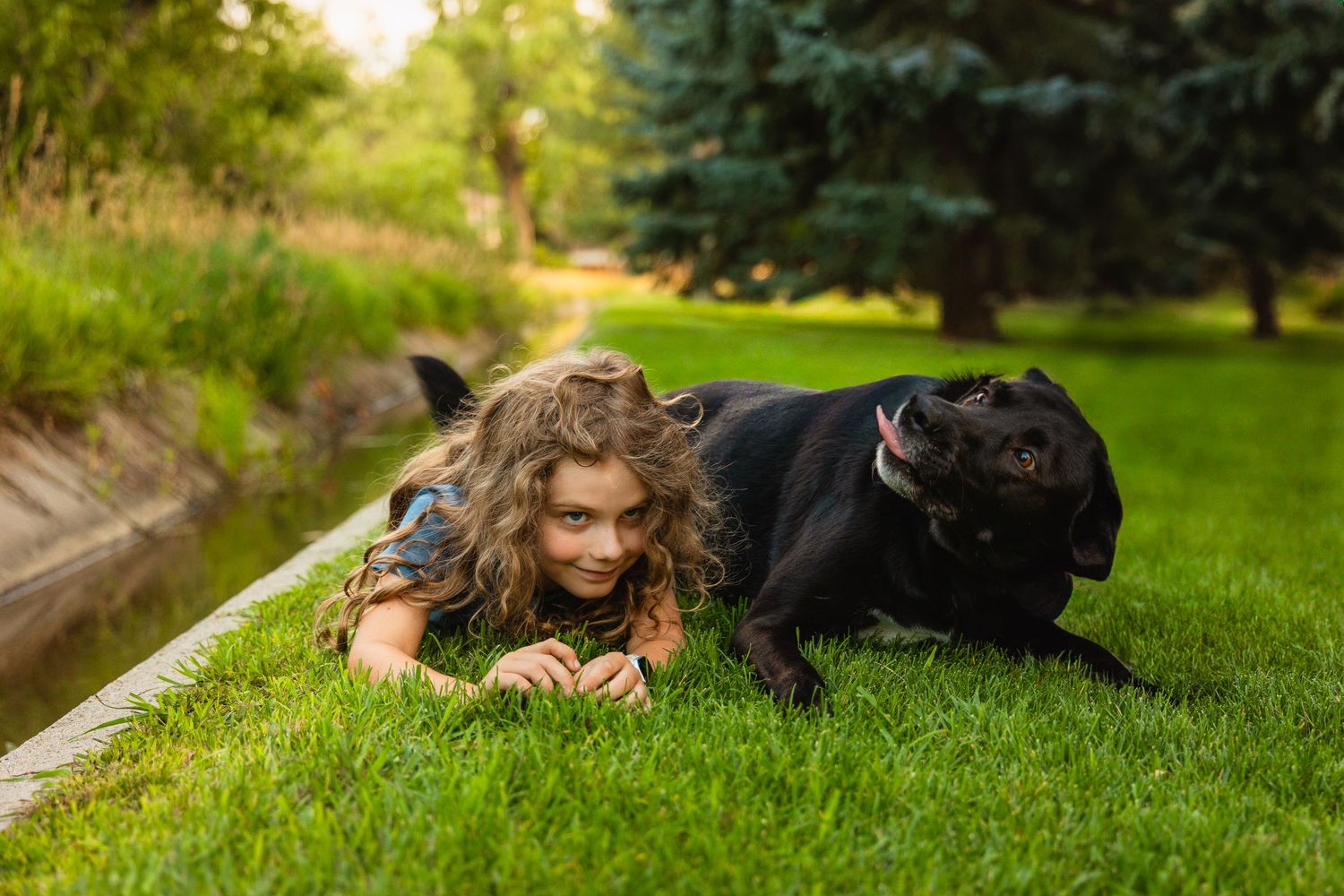 A child lying in the grass next to a large black dog on a warm summer day.