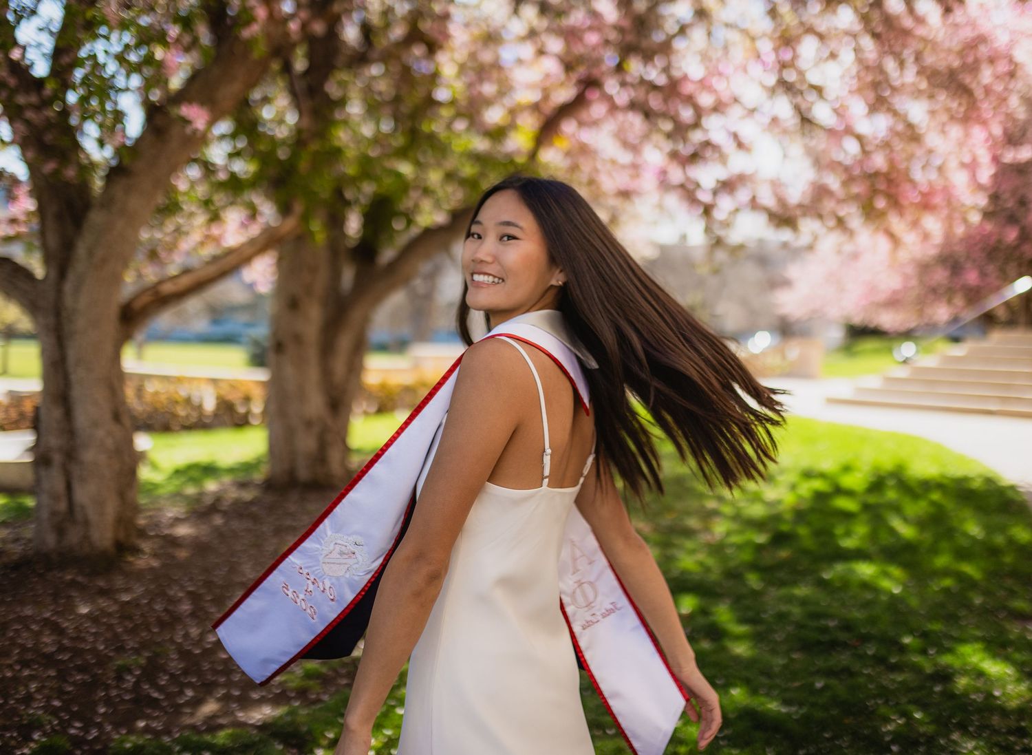 A series of photos showing someone in a white dress twirling under blooming cherry blossom trees in springtime.