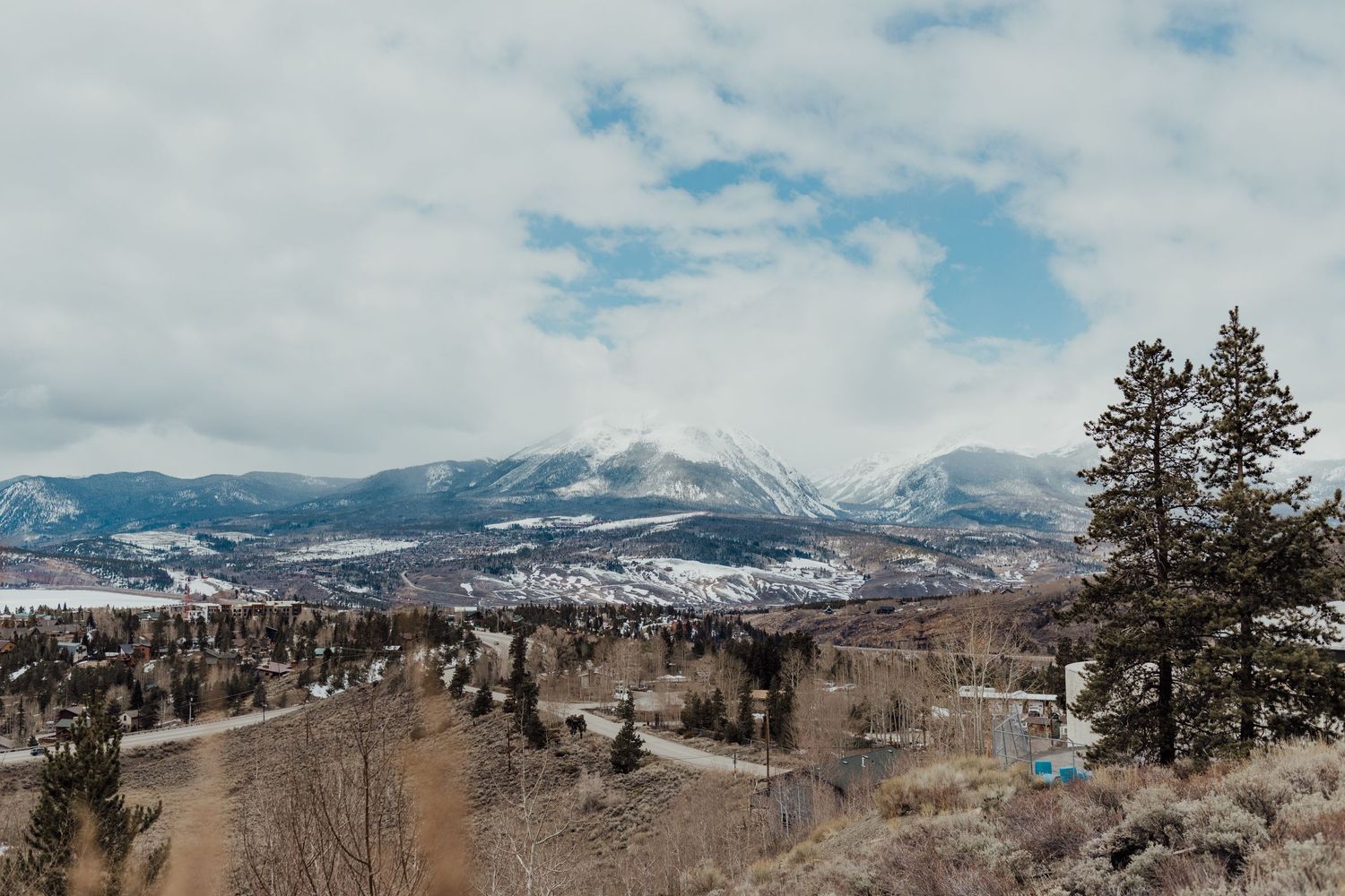 Snow-capped mountains and valley landscape under cloudy blue sky.