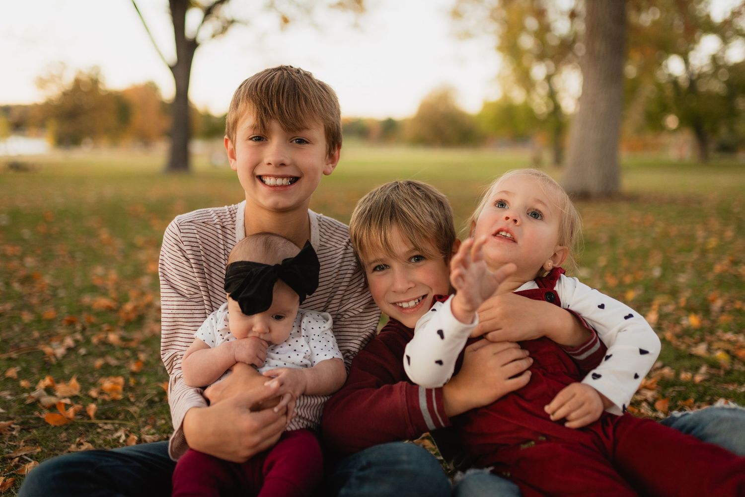 Three children sitting on fallen autumn leaves in a park at sunset with kittens during golden hour.