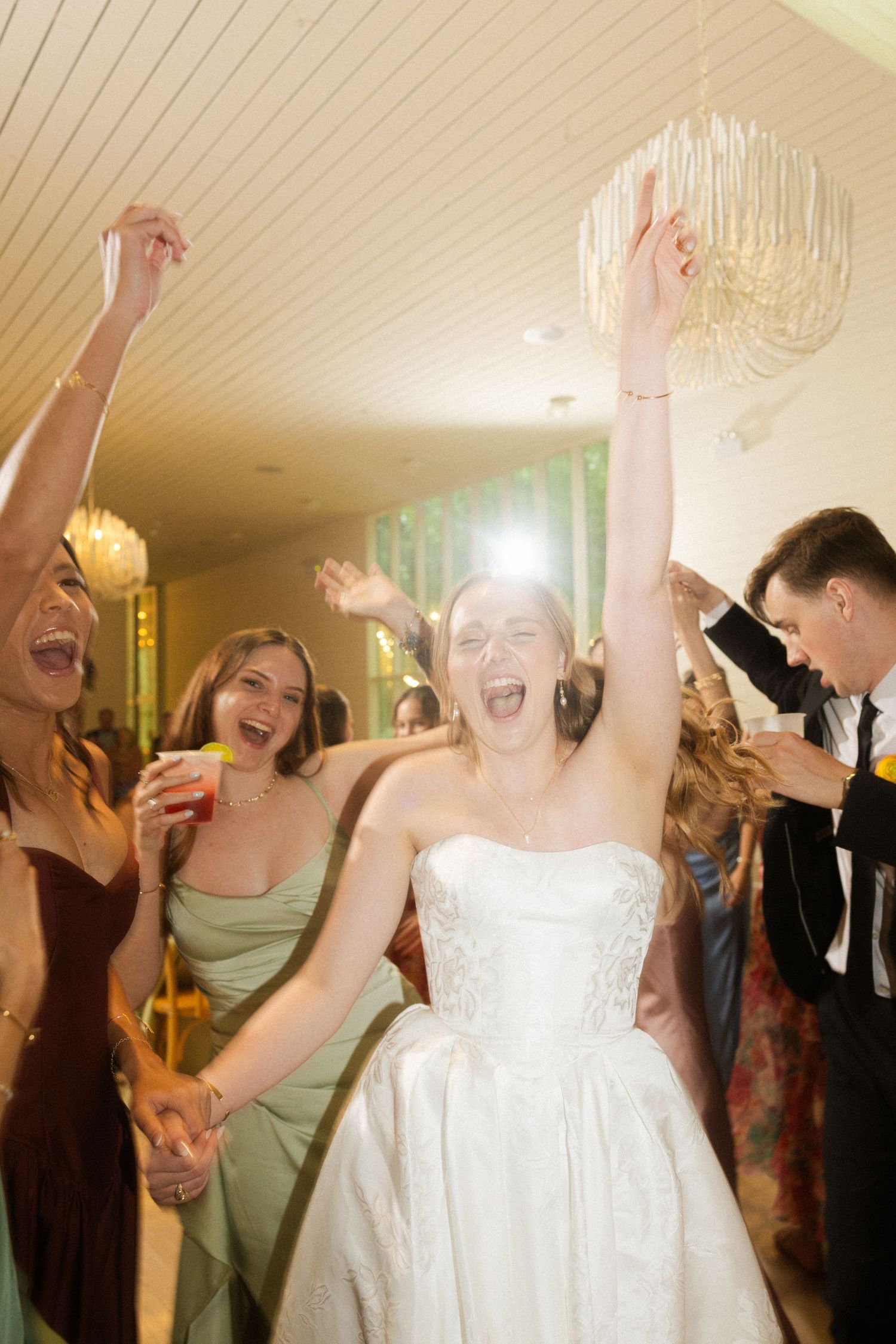 Joyful bride in white gown dancing with arms raised at lively wedding reception celebration.