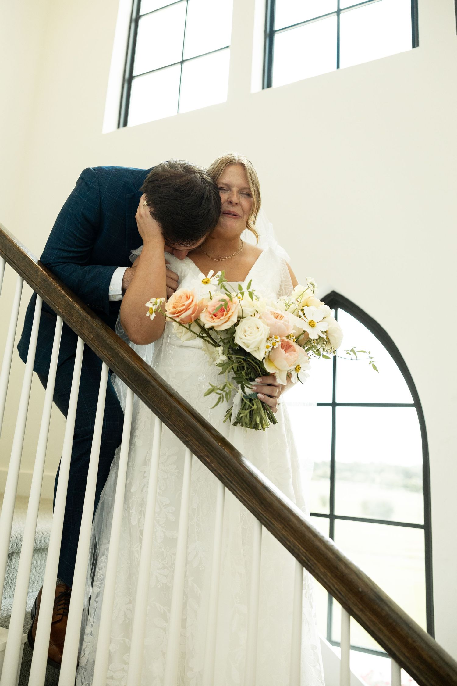 Elegant wedding couple poses on staircase with natural window lighting.