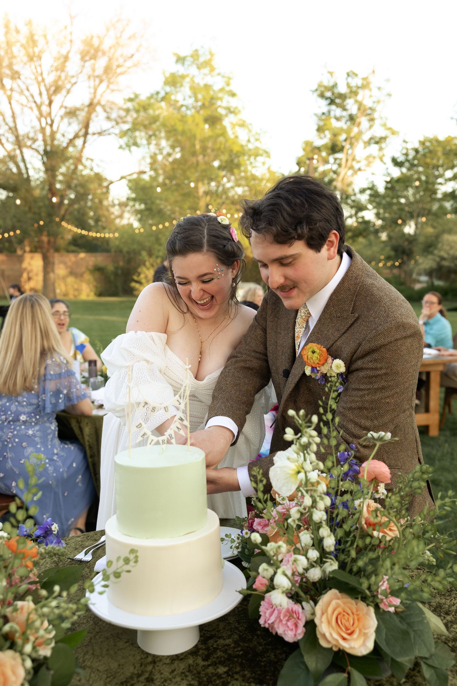 Newlyweds share a laugh while cutting their elegant mint green wedding cake surrounded by floral decorations.
