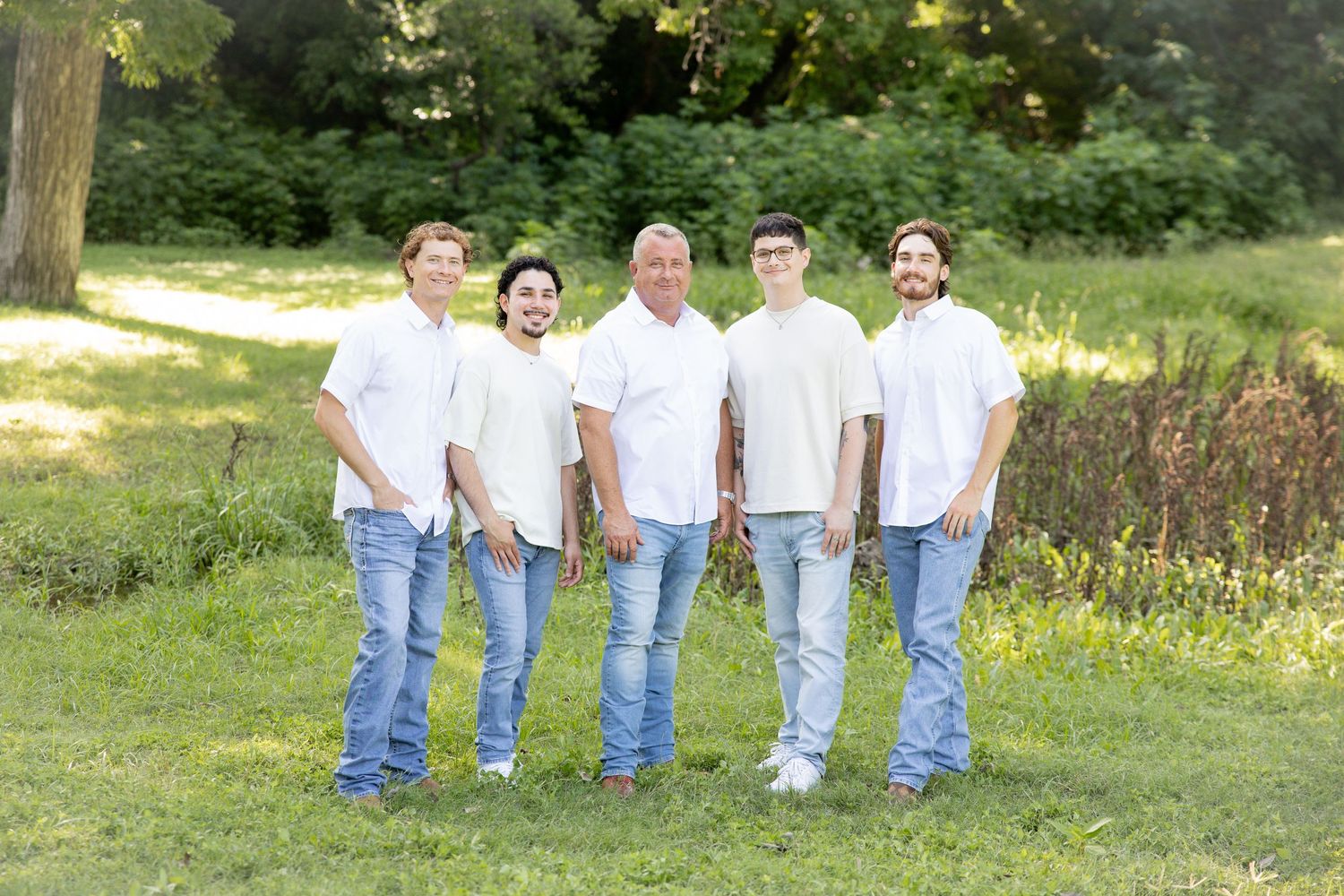 Family group wearing coordinated white shirts and jeans poses in a sunny meadow.