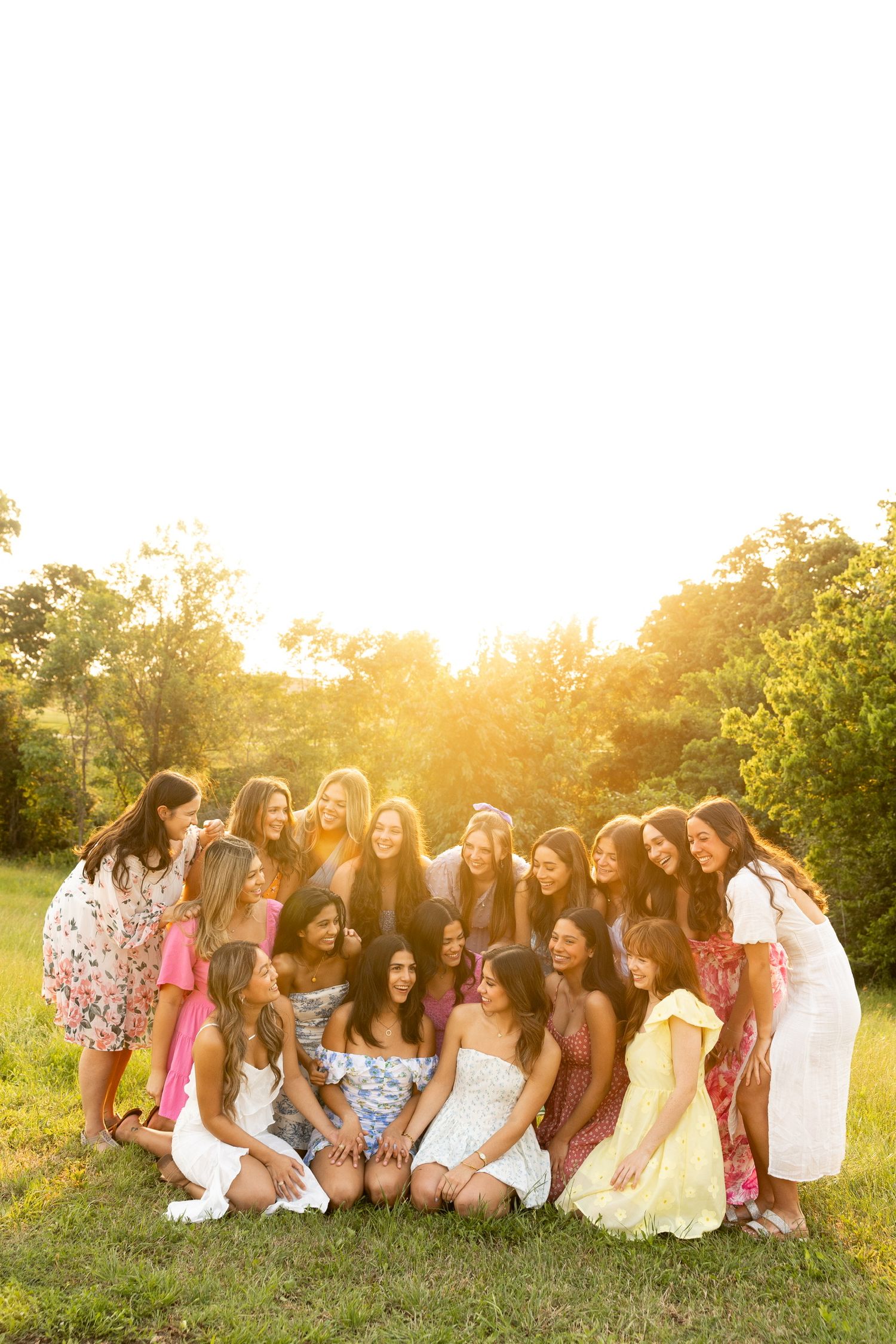 Group sits together on grass during golden hour surrounded by trees.