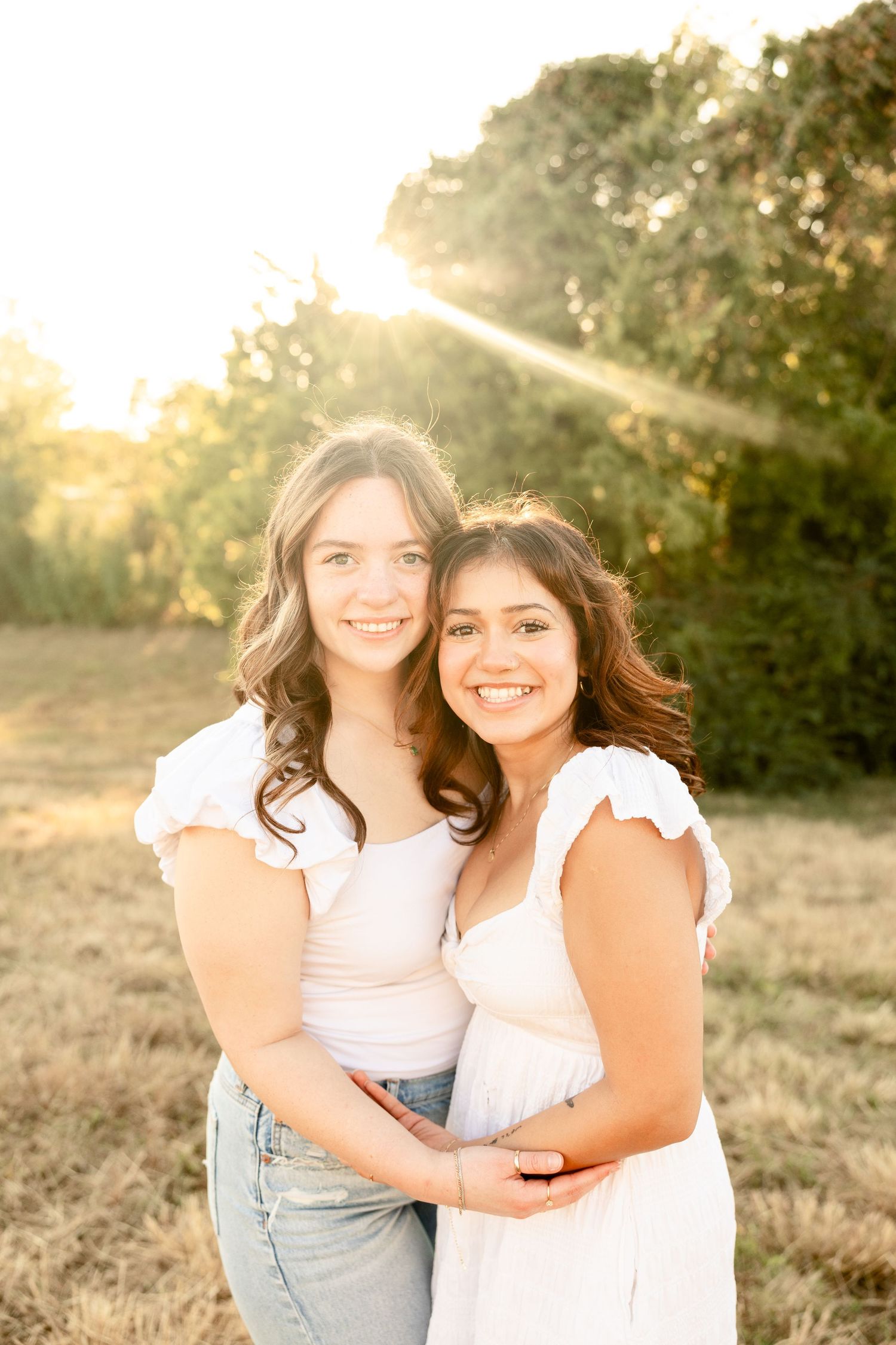 Two friends embracing in white outfits during golden hour photoshoot.
