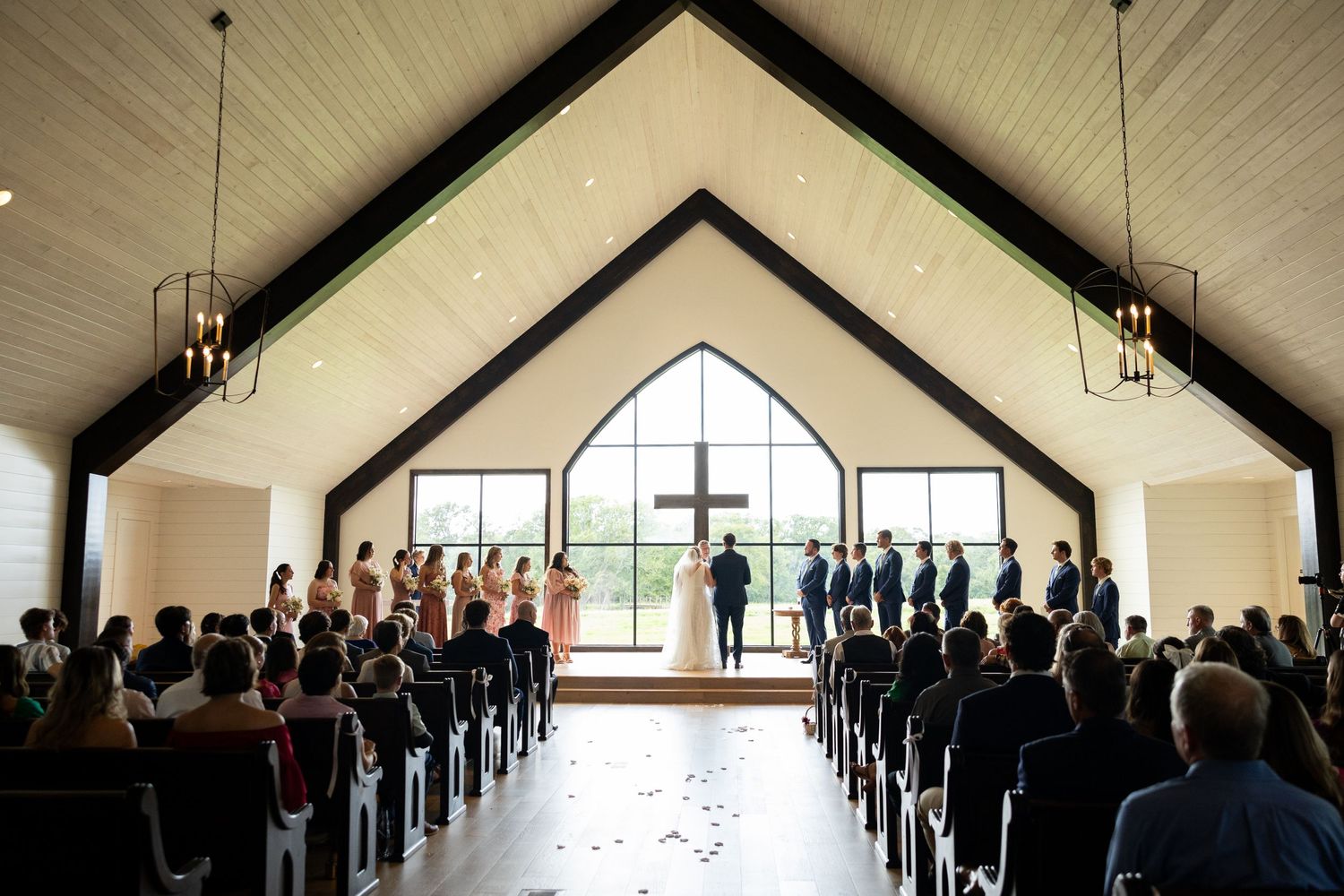 Wide angle view of wedding ceremony in minimalist chapel with guests.