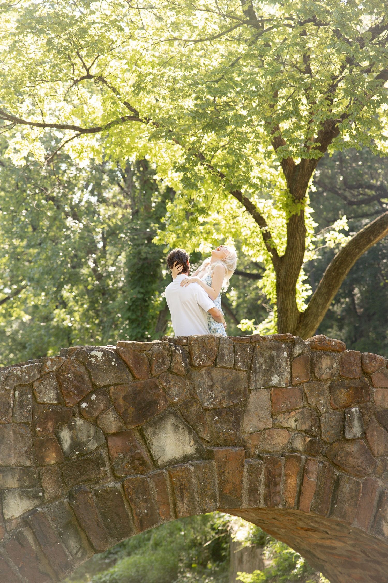 Romantic portrait on stone bridge with sunlight filtering through summer foliage.