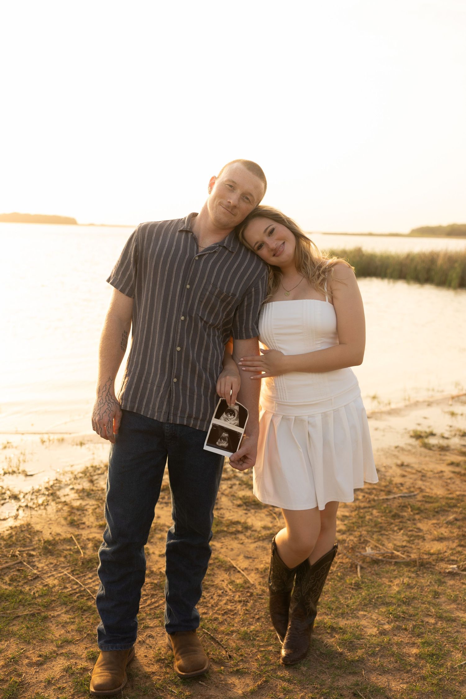 Couple posing with ultrasound photos during sunset beach photography session.