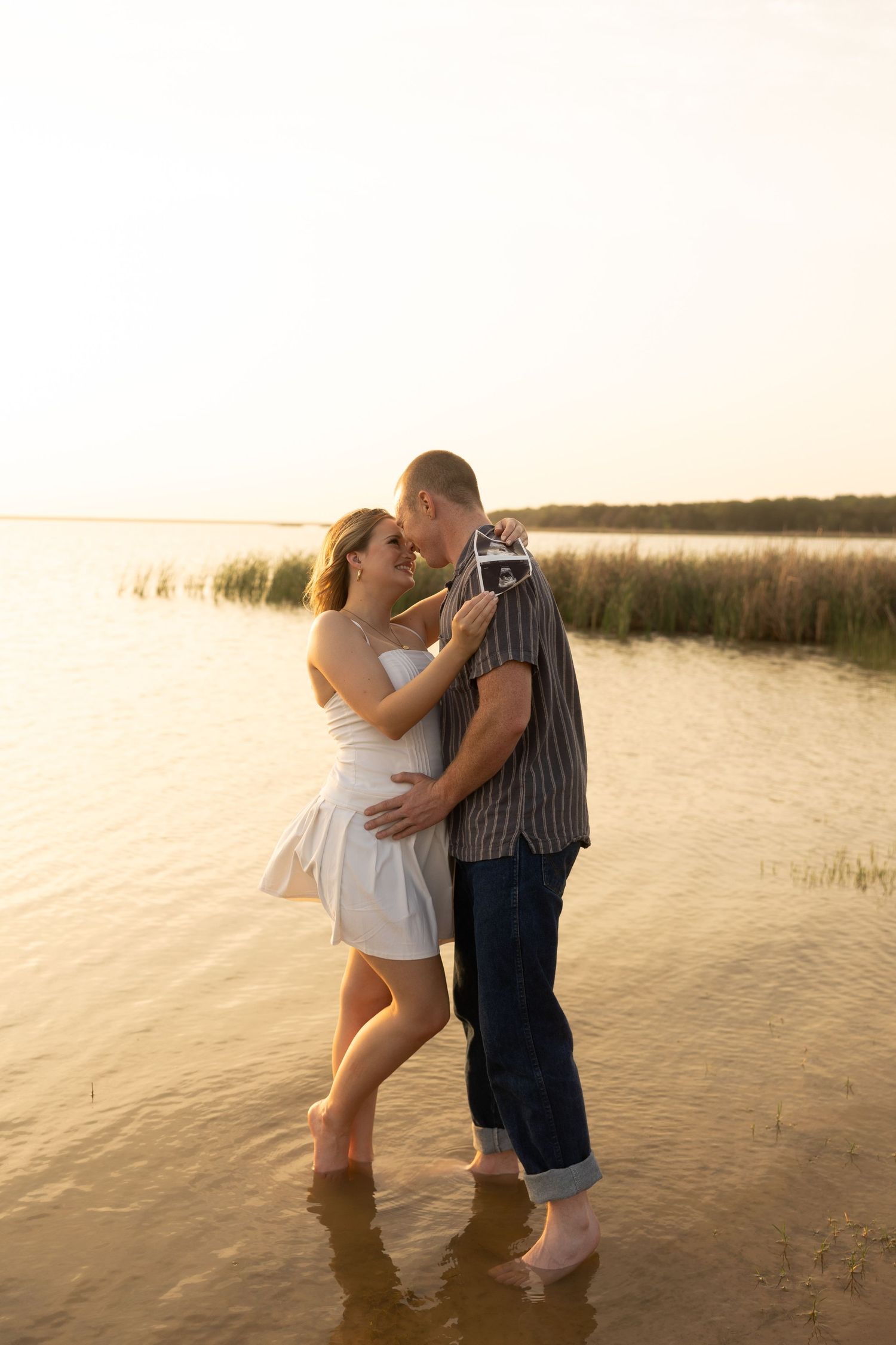 A romantic couple embraces in shallow water during golden hour.