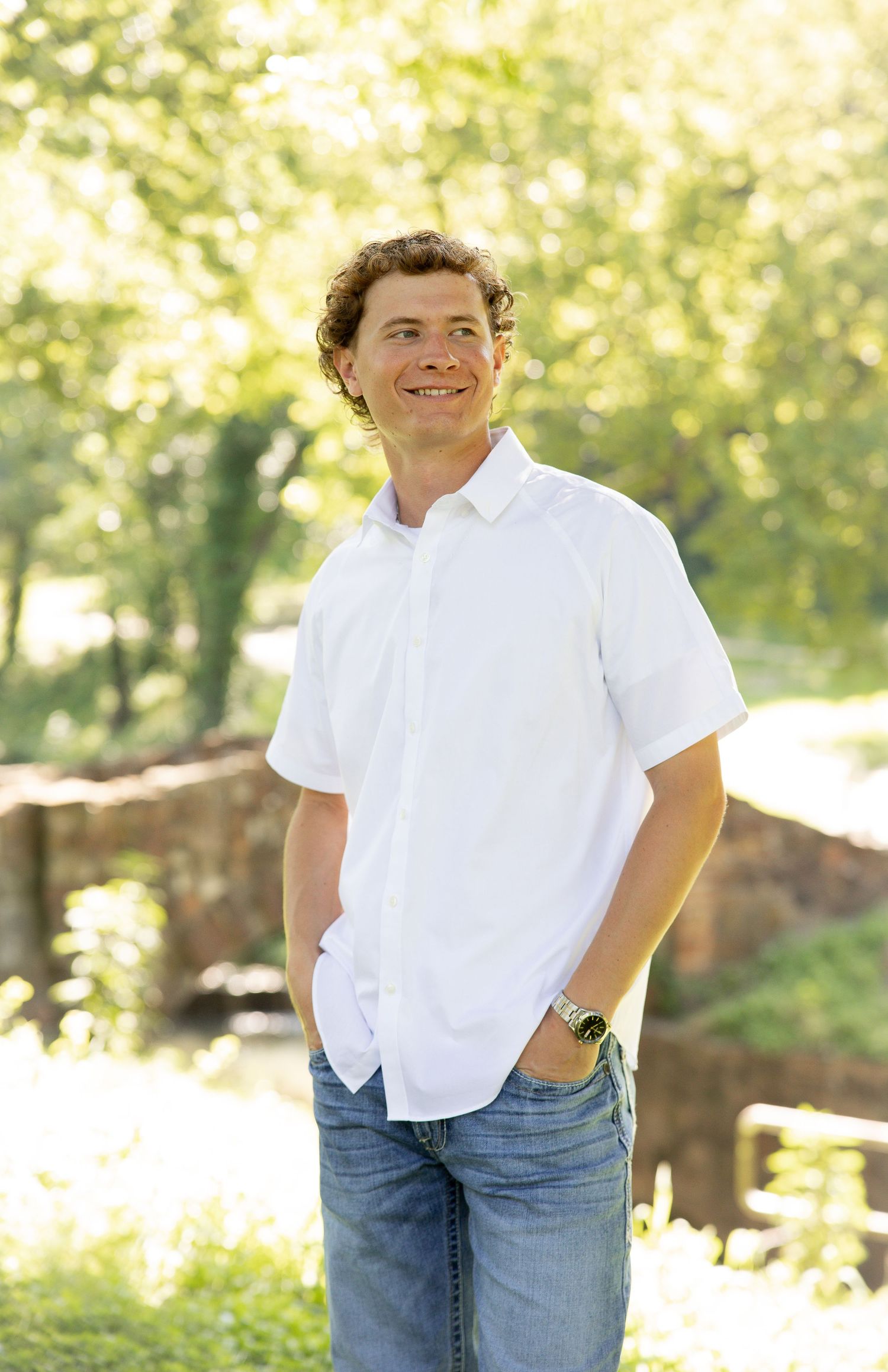 Casual portrait in white shirt and jeans against a sunlit garden background.