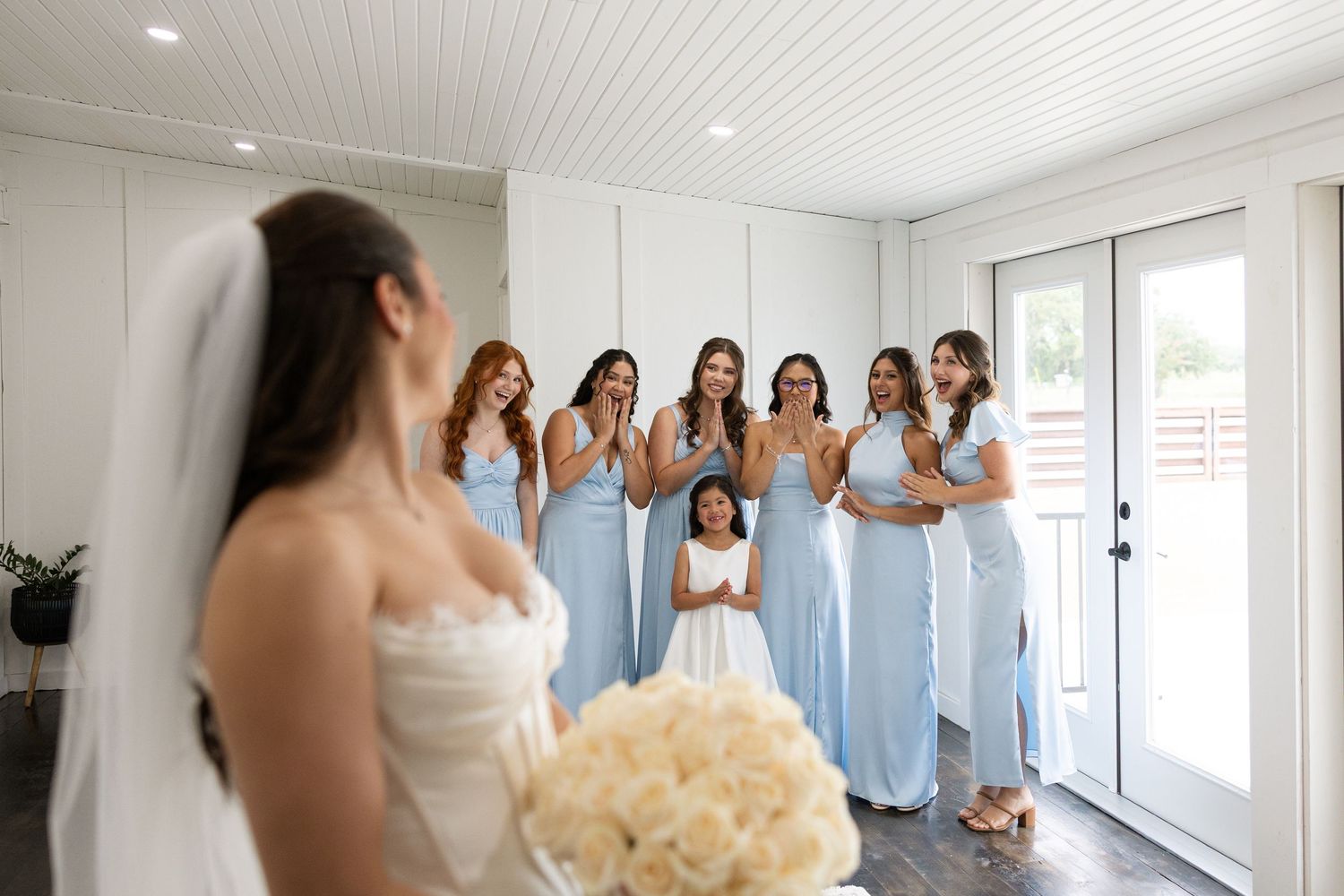 Bridesmaids in flowing light blue dresses admire the bride in her wedding gown.