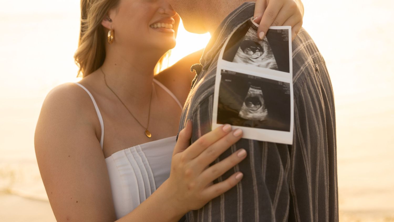 Romantic sunset beach photoshoot with ultrasound photos being shared on the shoreline.