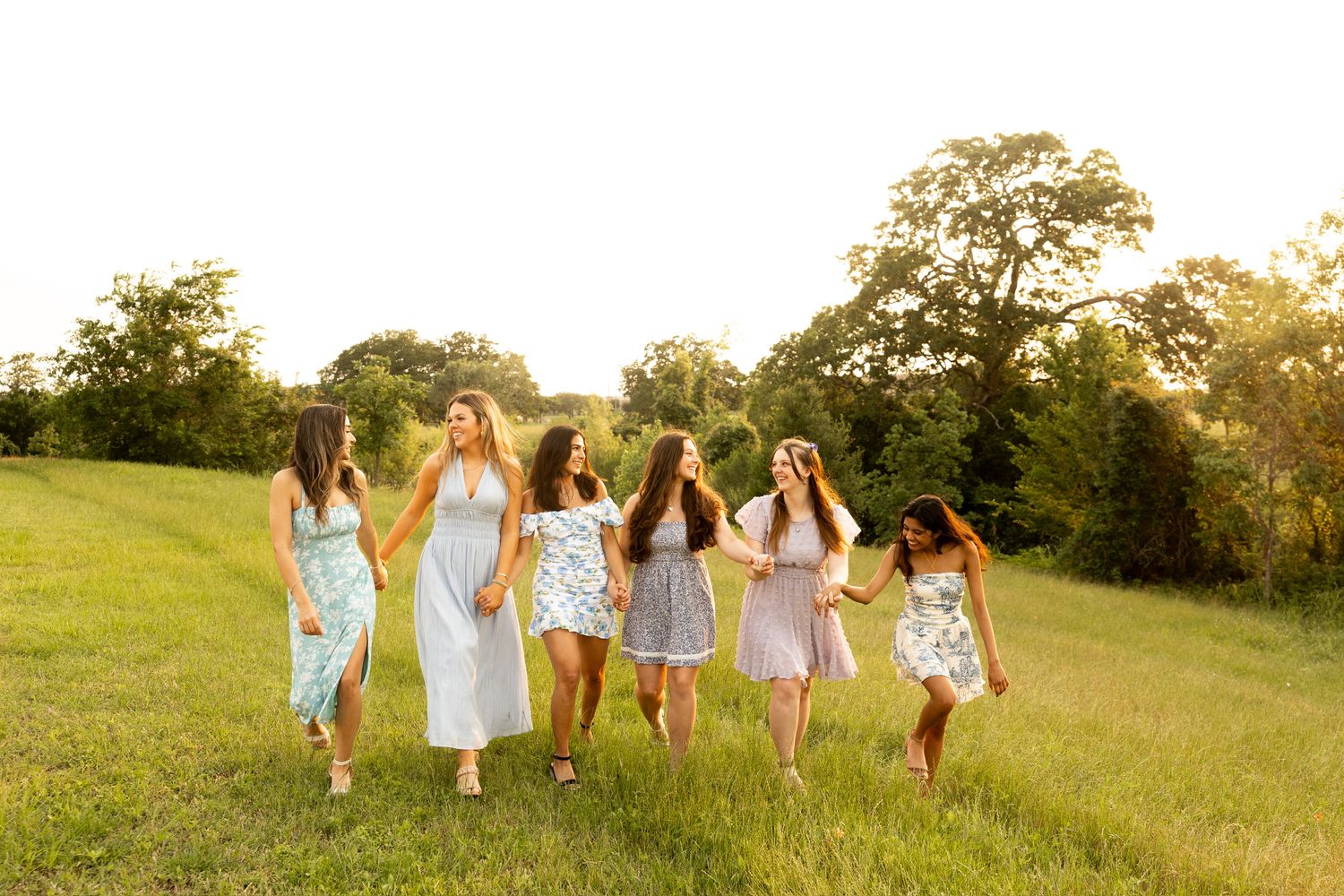 Group walks together through a sunny field wearing pastel summer dresses.