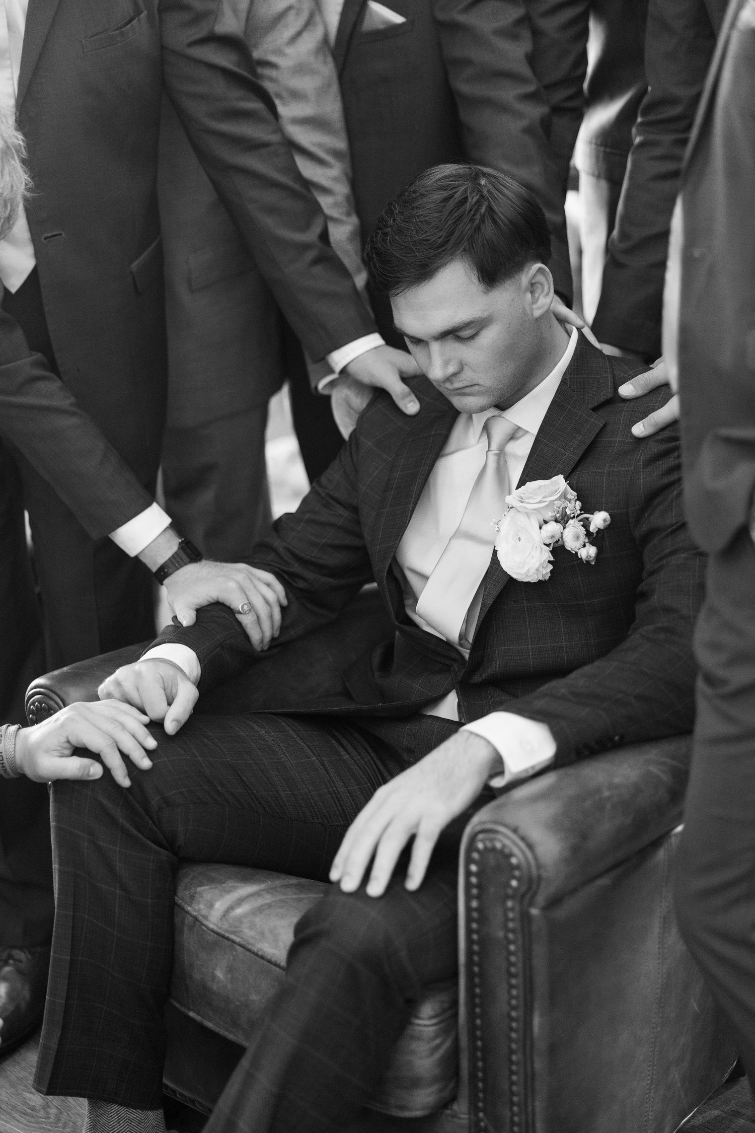 Men in formal suits seated on leather chairs during wedding event.