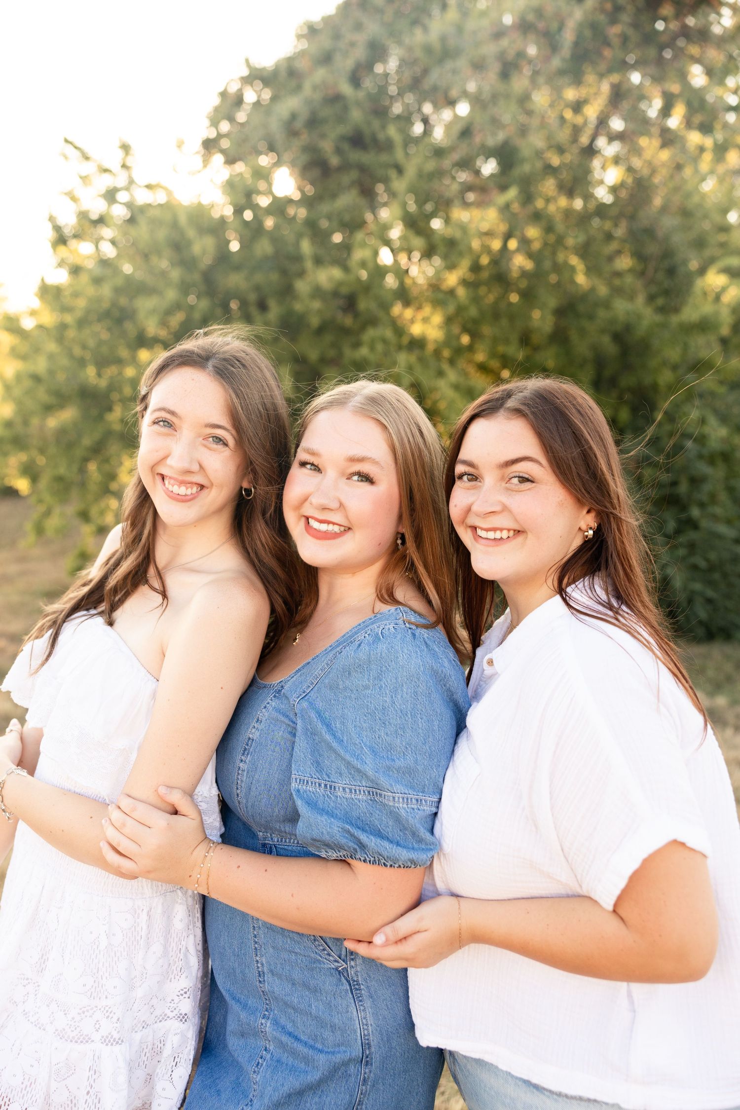 Three friends in casual outfits smiling together during sunset photoshoot.