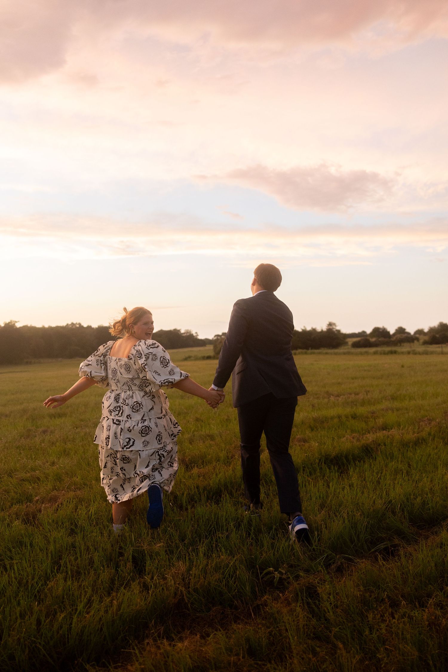 Couple holding hands while running through meadow at golden hour.