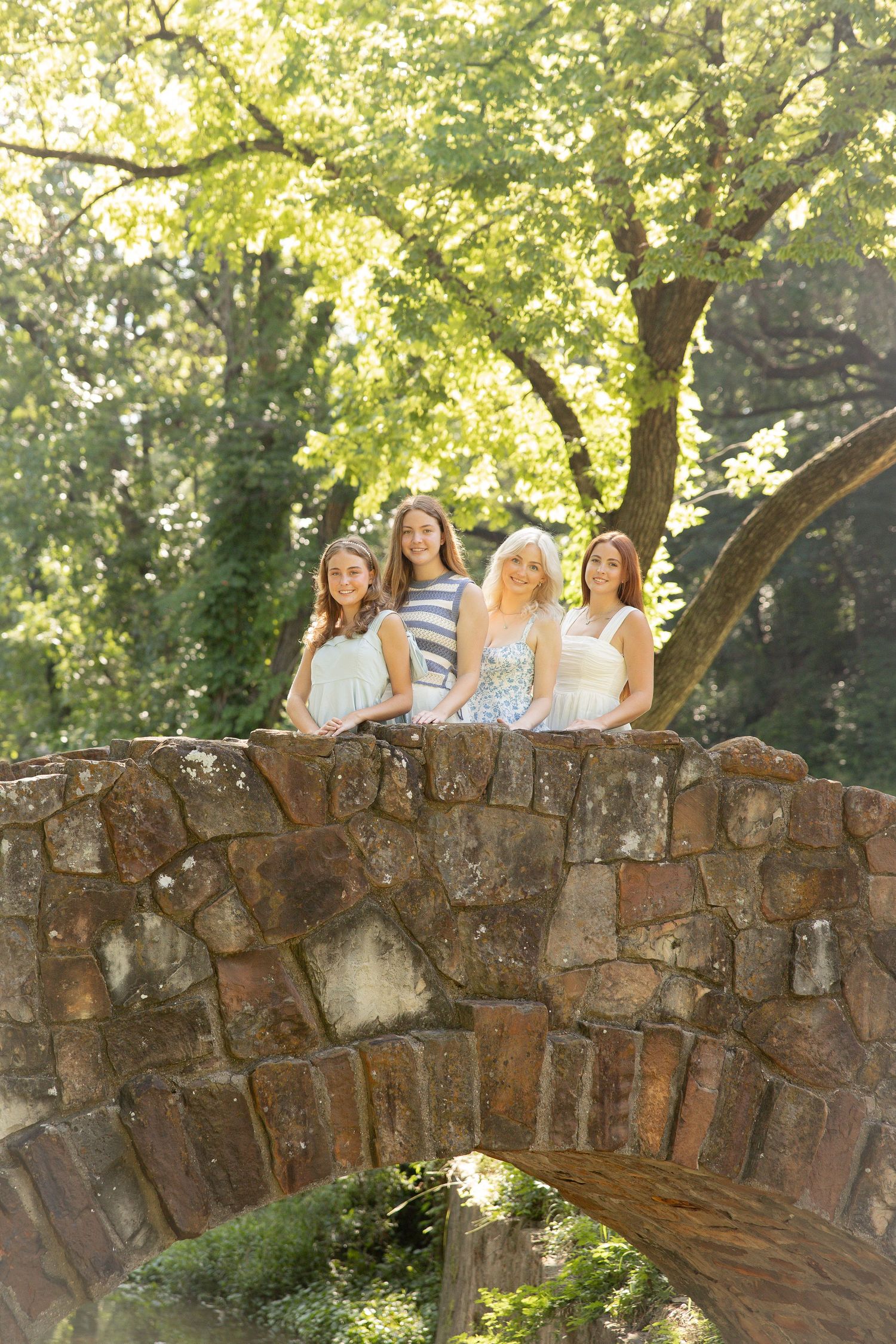 Group photo taken on a rustic stone wall surrounded by lush green trees in natural lighting.