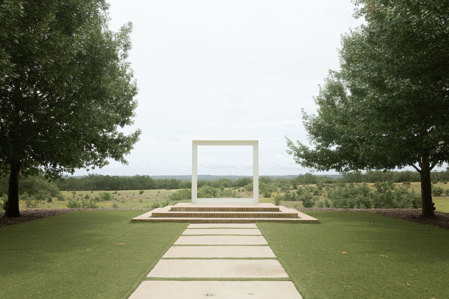 Elegant outdoor wedding arch on manicured lawn flanked by trees with scenic countryside views.