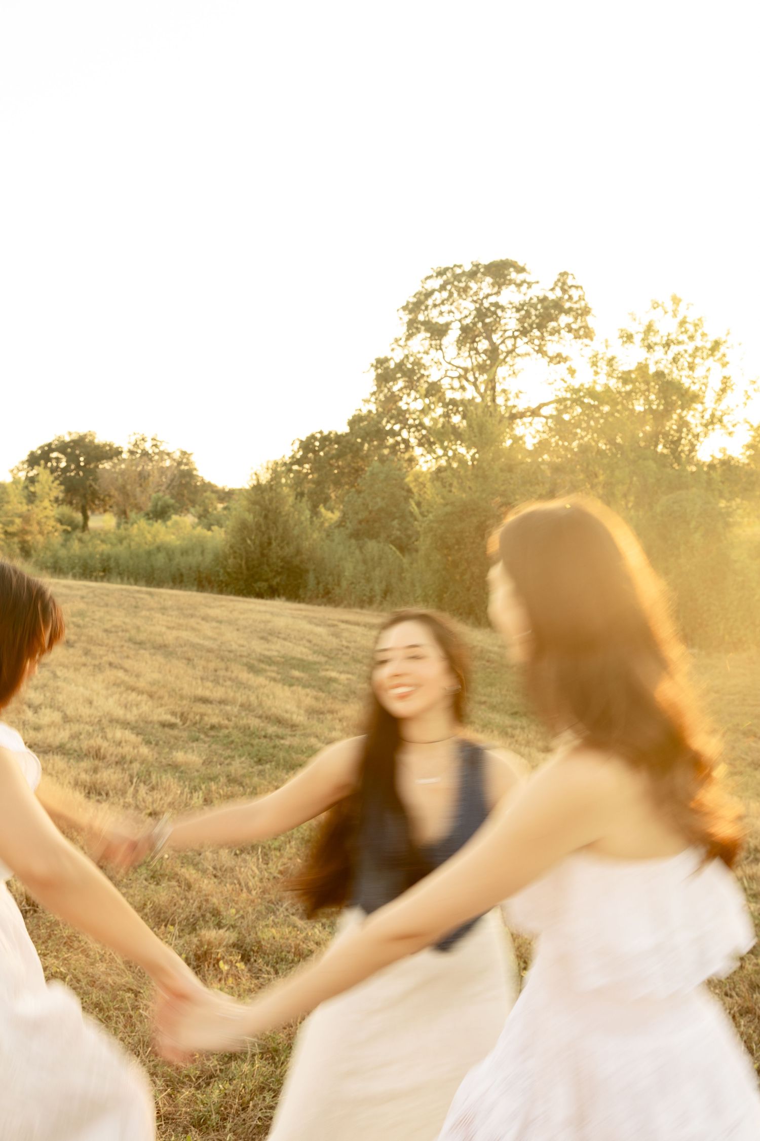 Friends twirling and dancing together in a golden field at sunset.