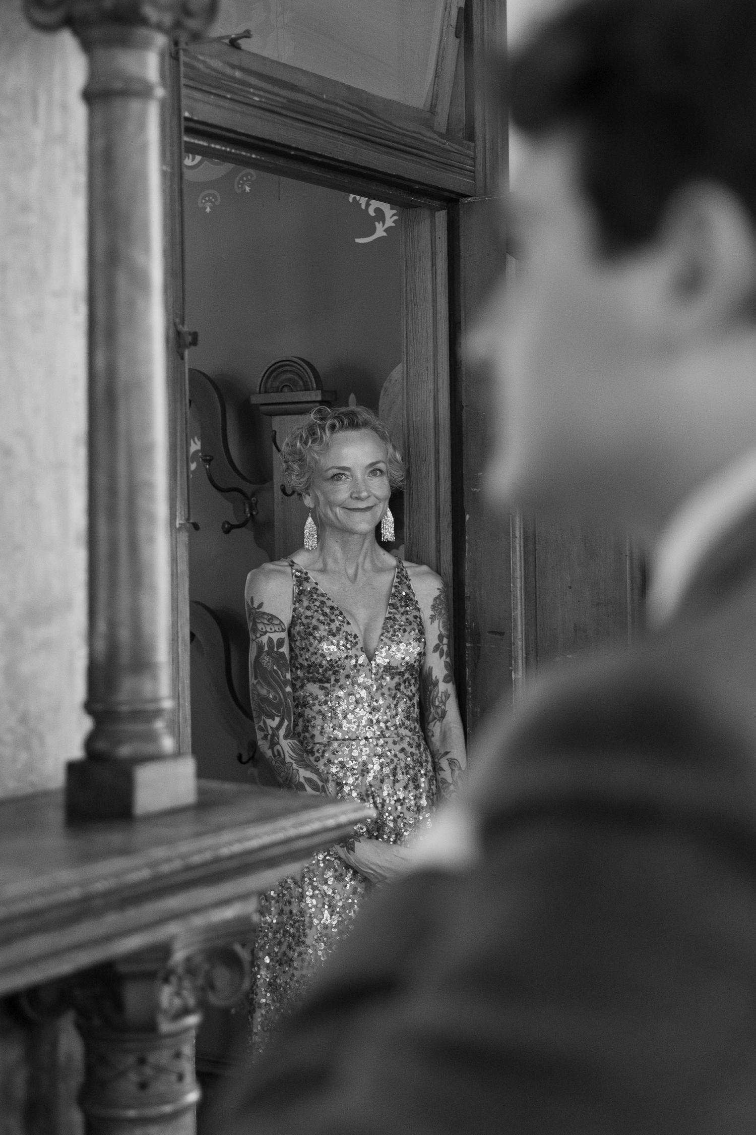 A reflection in an ornate mirror shows a woman in a sparkly dress during a wedding celebration.
