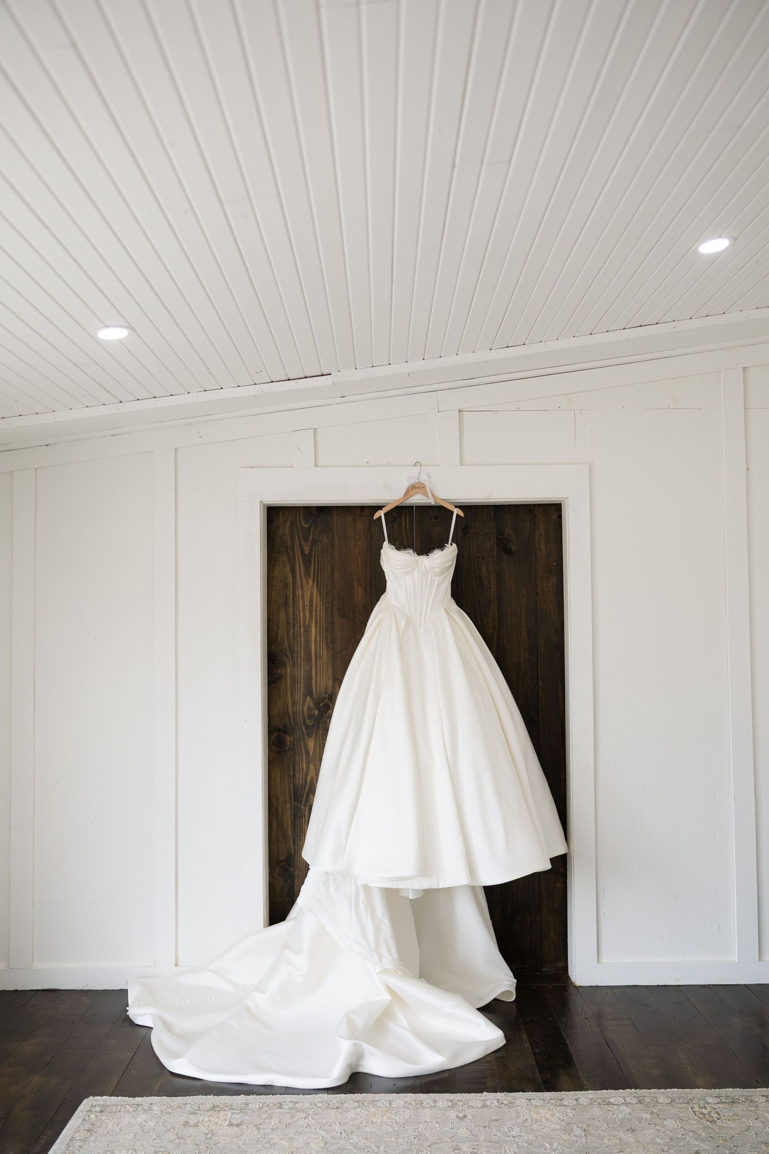 A beautiful white wedding dress displayed against dark wooden panels in an elegant room.