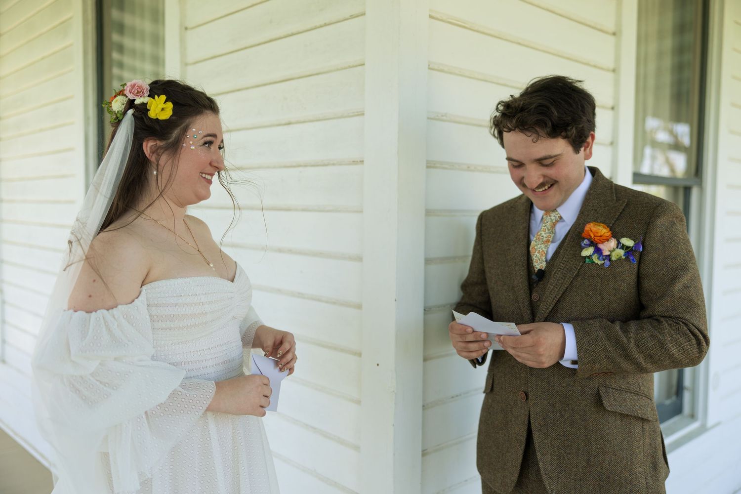 A wedding couple exchanges vows on a white porch while dressed in traditional attire.